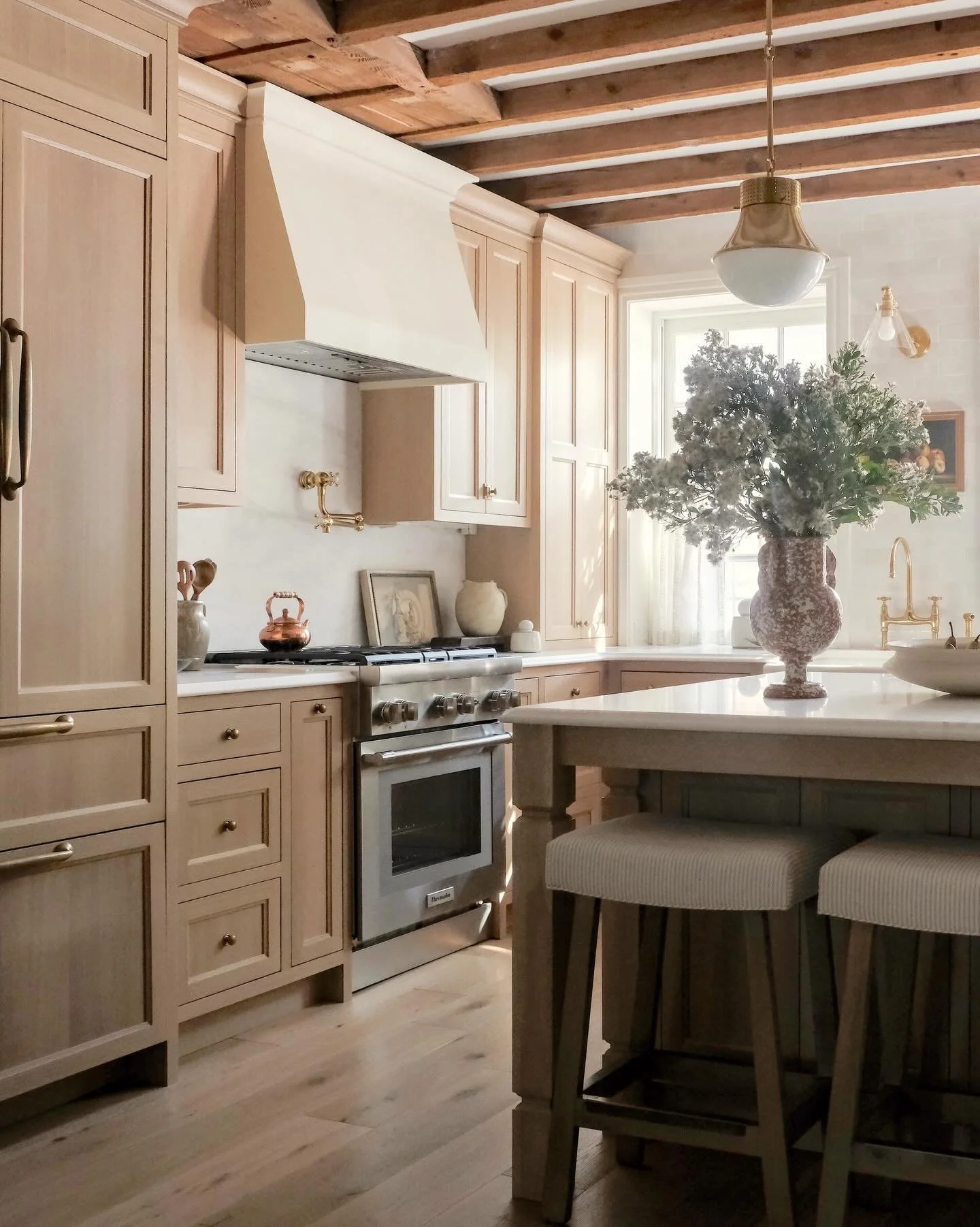 A kitchen where warmth meets elegance &mdash; soft neutral cabinetry, timeless brass details, and rustic ceiling beams creating a space that feels both refined and inviting. Designed for slow mornings, shared meals, and everyday beauty. 
📷: @rmcginn