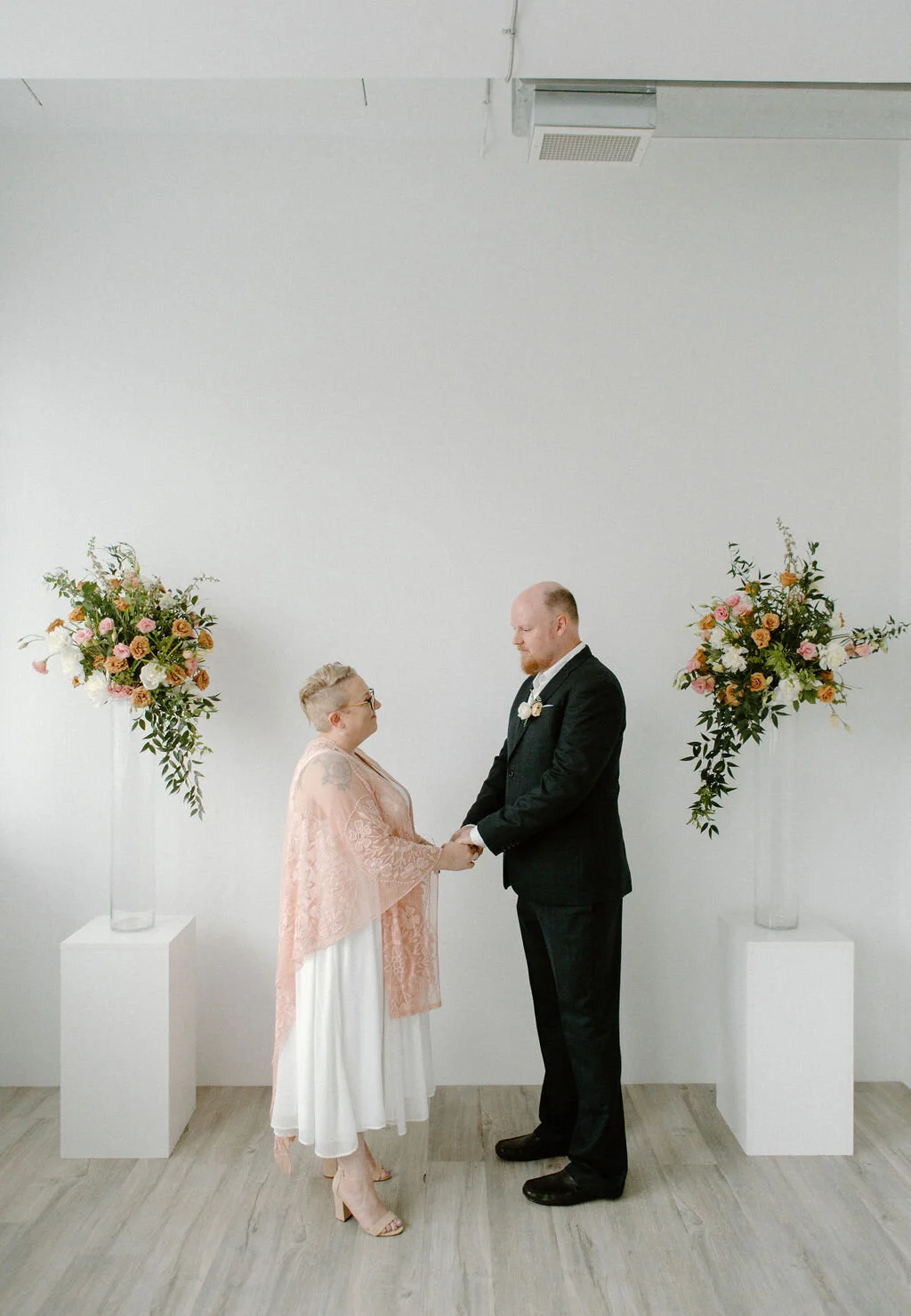 Bride and groom standing at the alter. Two white square box pillars have two floral arrangements I Elopement in Kitchener Waterloo by CK &amp; Co Events