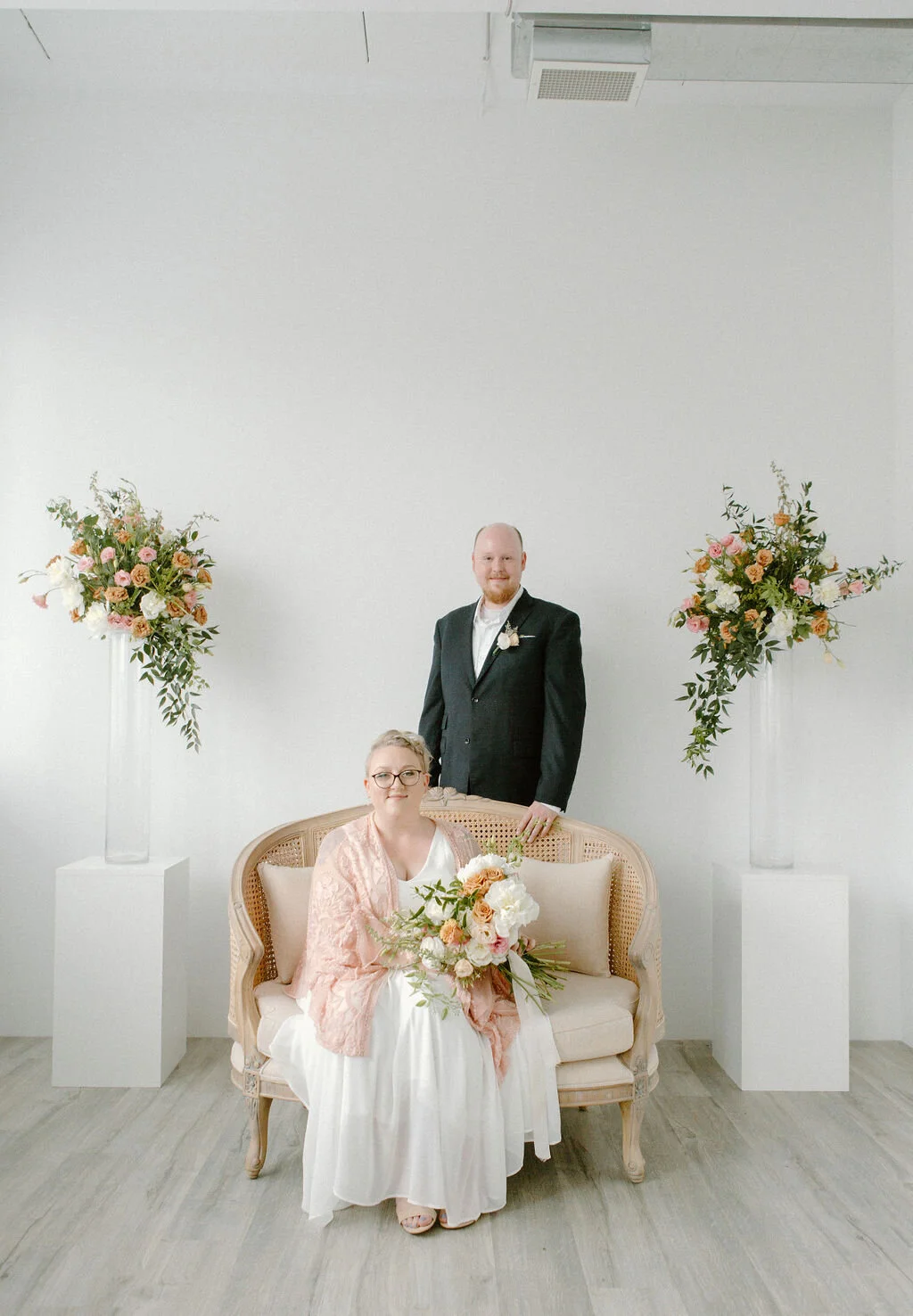 Bride sitting on a gorgeous pink sofa with groom standing behind her I Elopement in Kitchener Waterloo by CK &amp; Co Events