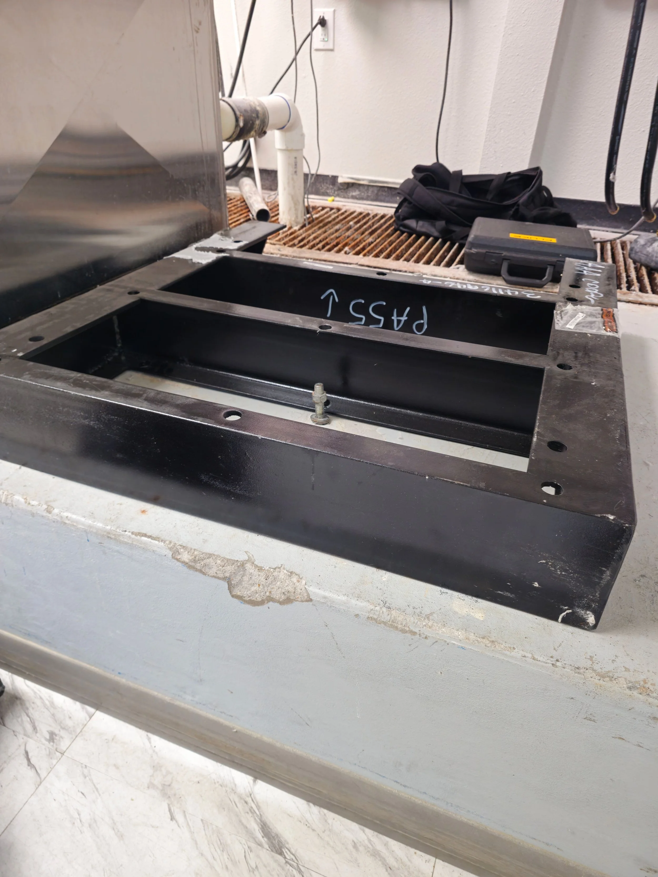 A black metal frame on a workbench marked with the word 'PASS' and an upward arrow, with a bolt and wrench nearby, in a workshop or industrial setting.