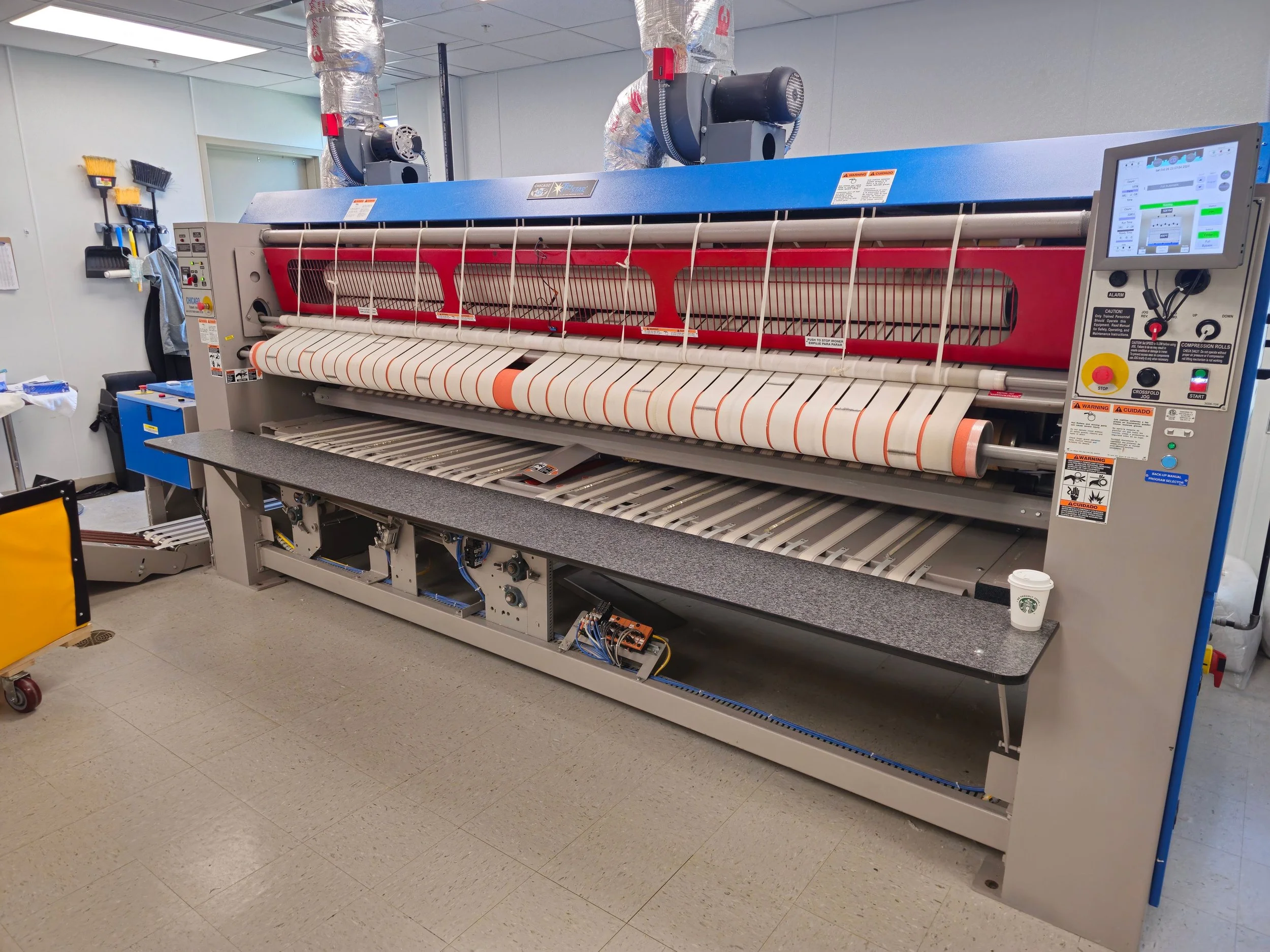 Commercial fabric cutting machine in a textile manufacturing room with a gray countertop and various tools mounted on the wall.