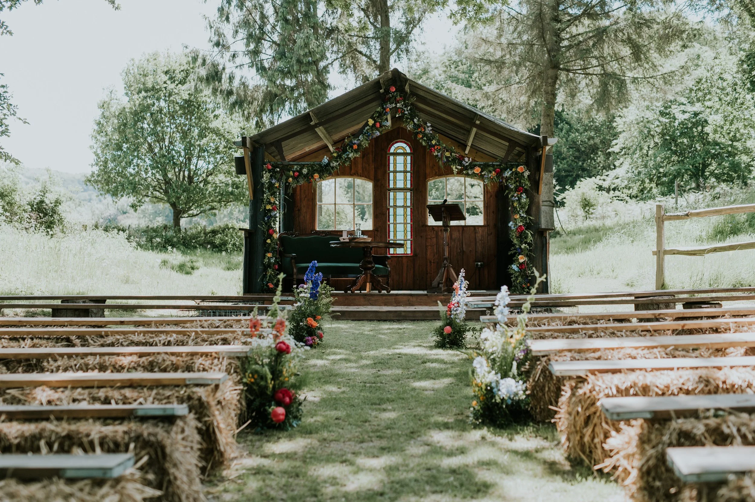Rustic outdoor wedding ceremony with wooden chapel, floral arch, hay bale seating and flower lined grass aisle Oak Tree Barn Tonbridge