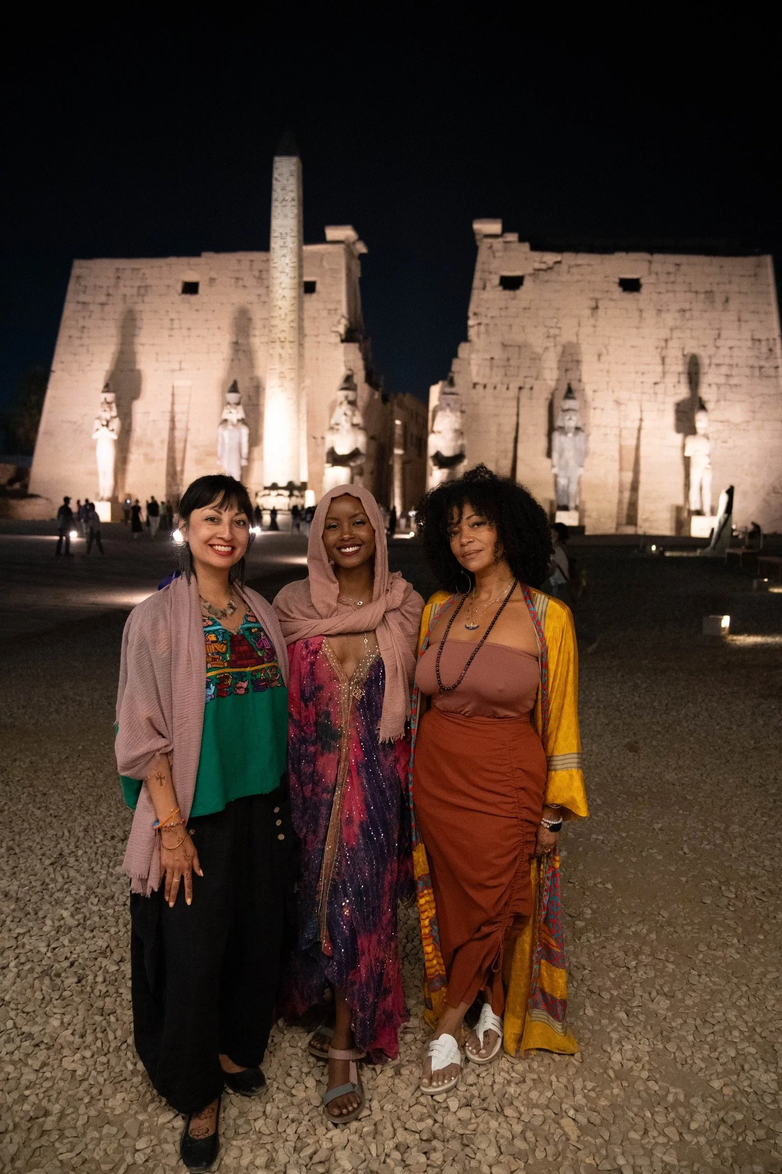 Three women standing in front of an illuminated ancient Egyptian temple at night.
