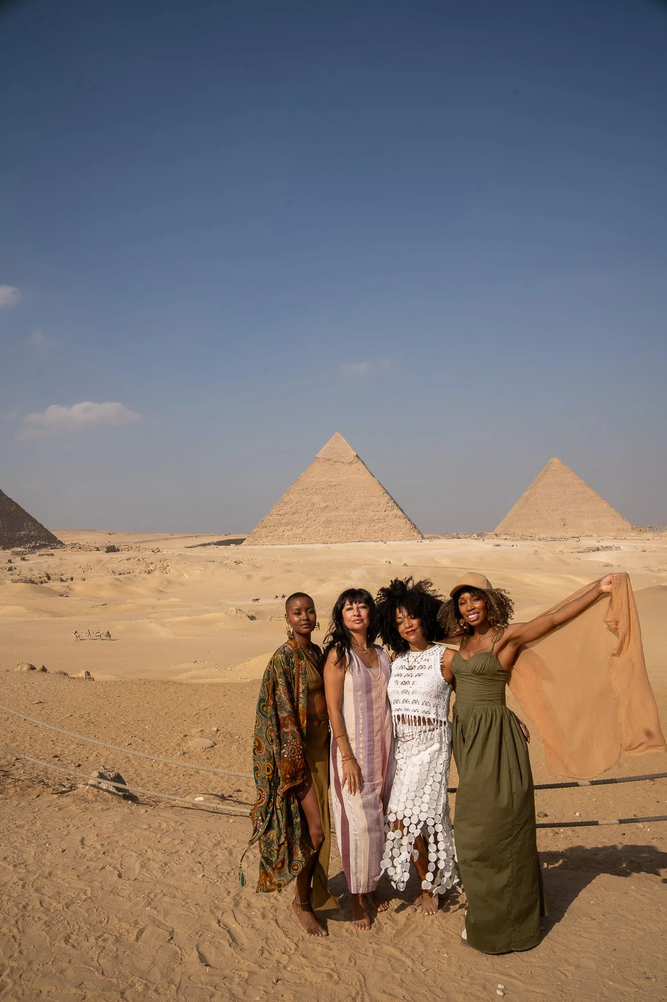 Four women standing with pyramids in the background in a desert.