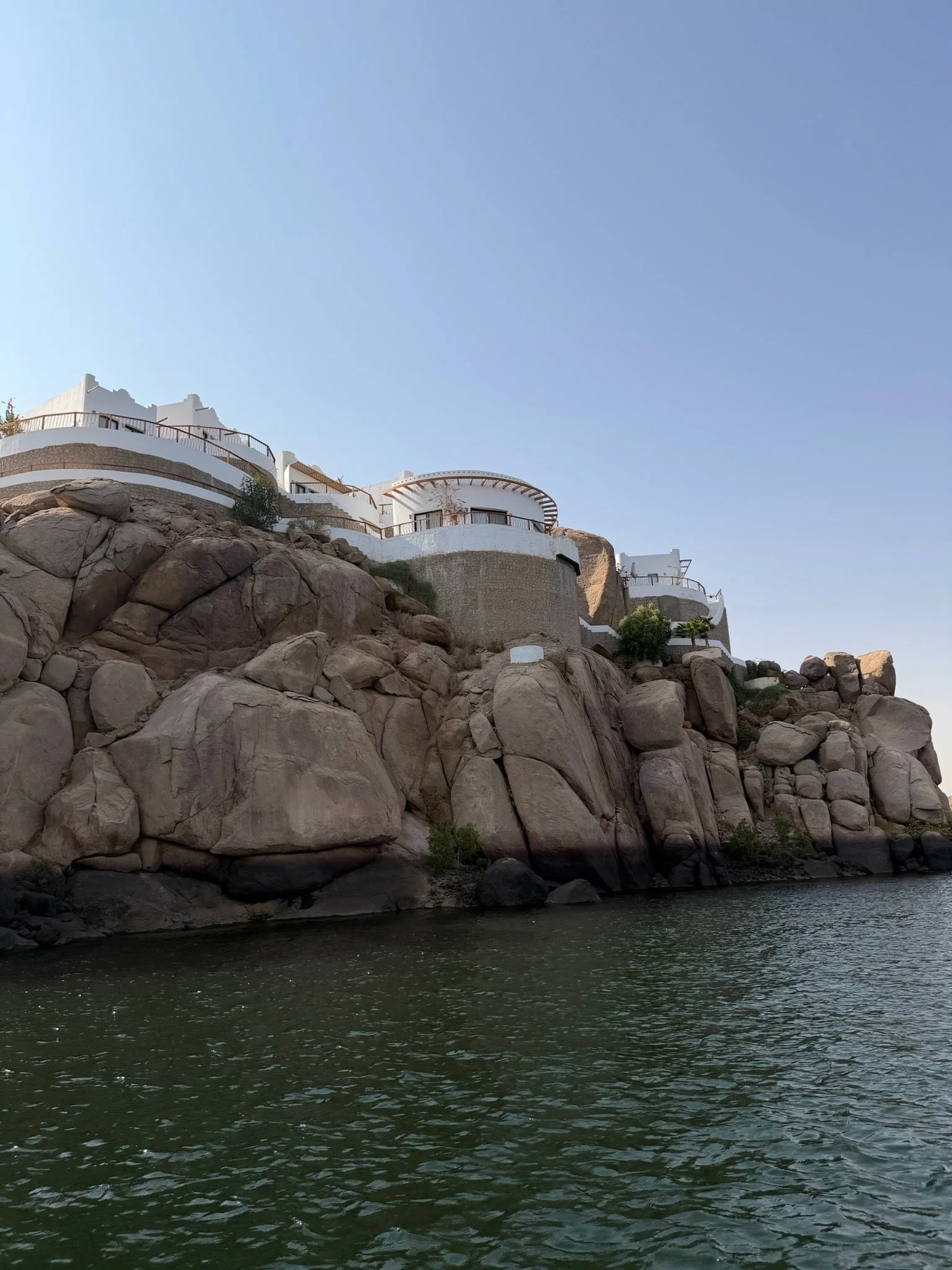 White buildings on a rocky cliffside overlooking a body of water under a clear blue sky.