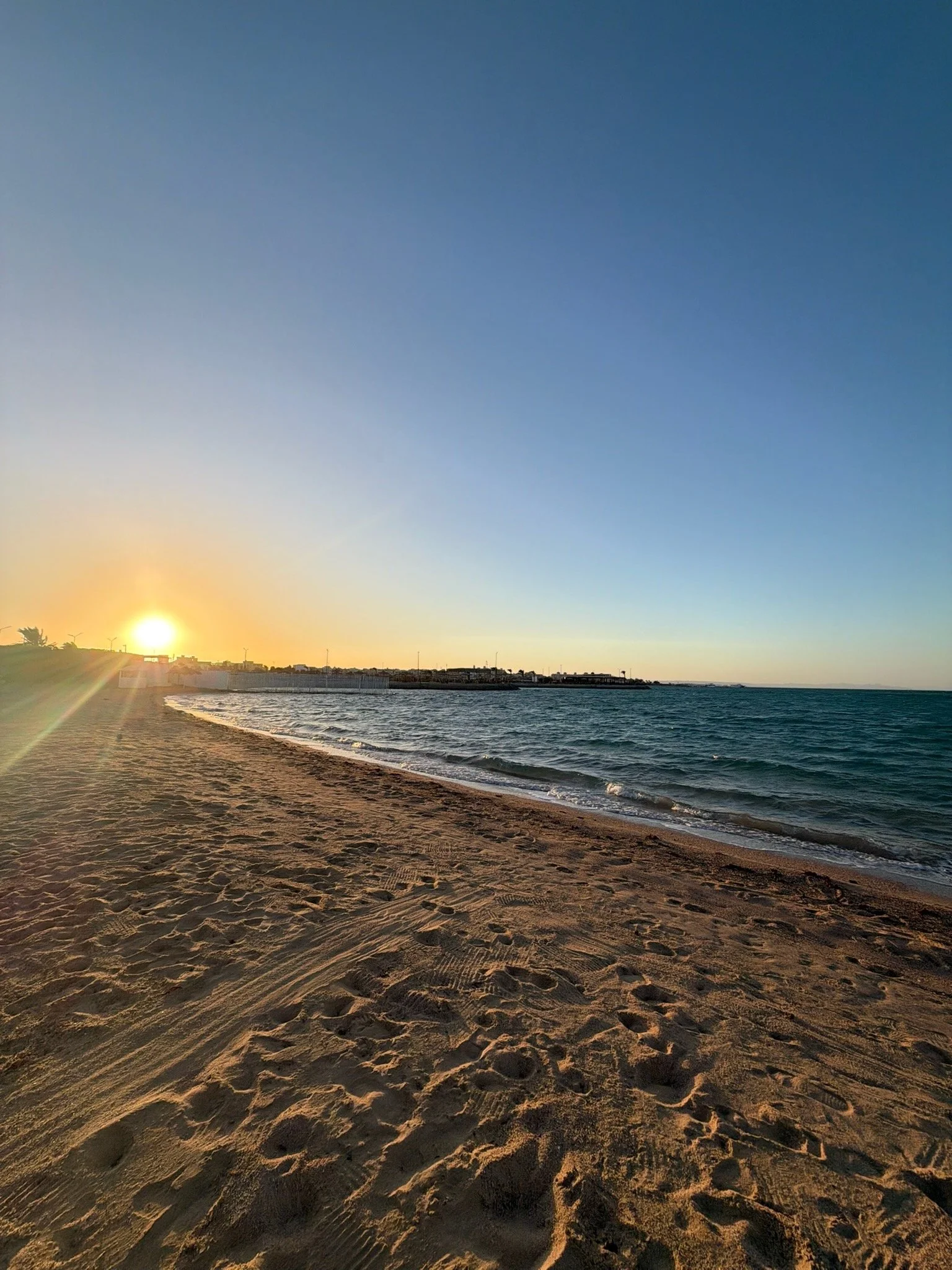 Sunset over a sandy beach with gentle waves and a cloudy sky.