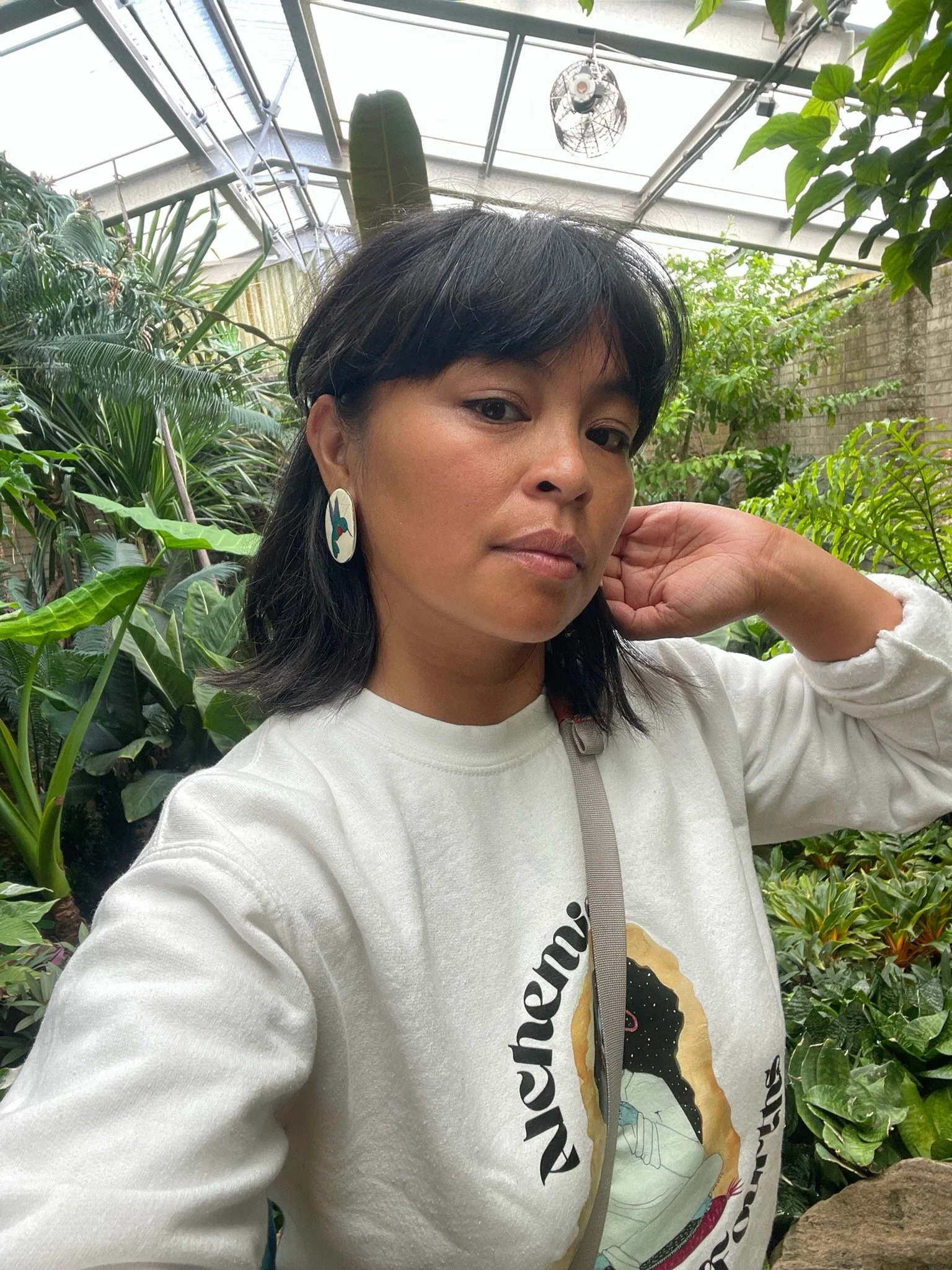 Wilorna with dark hair and a white shirt has foliage behind her