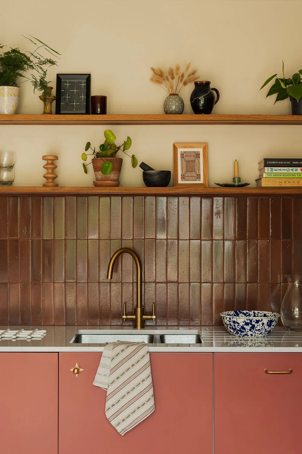 A contemporary kitchen in Knowle, Bristol with brown zellige backsplash tiles and oak open shelving with plants and ceramic objects. An antique brass tap and cabinet pulls add warmth and personality