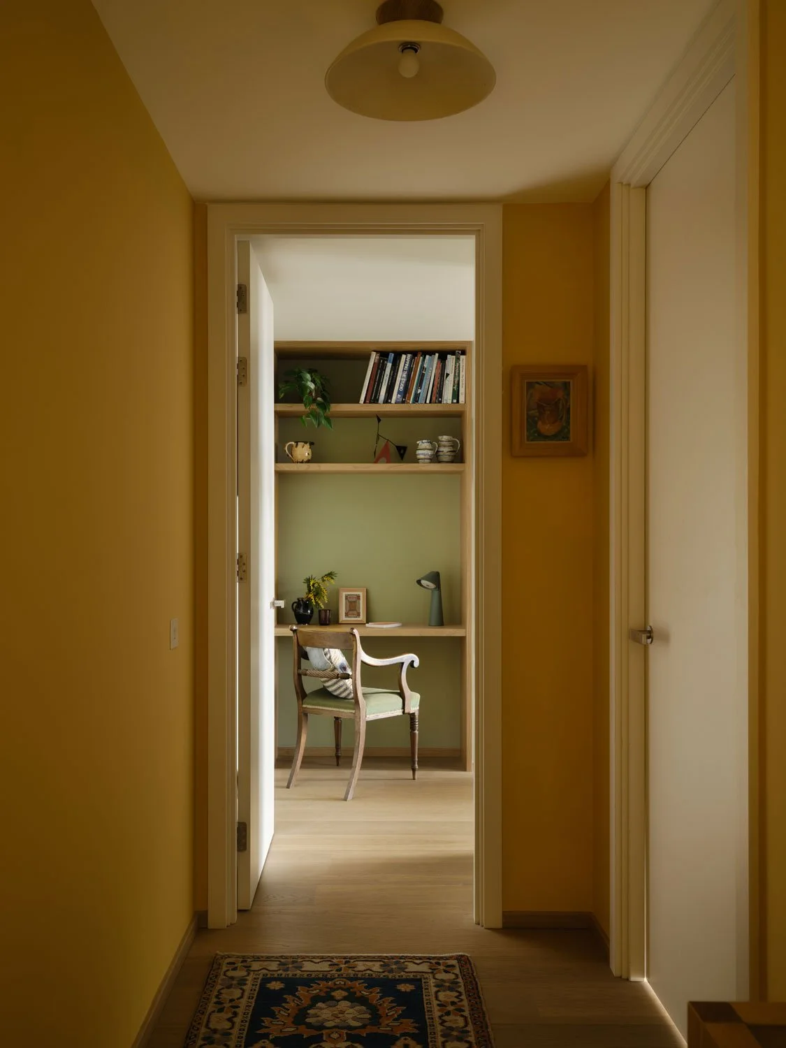 A view through to a dressing table nook from a warm ochre painted hallway. Artwork and ceramics add personality and charm to the space