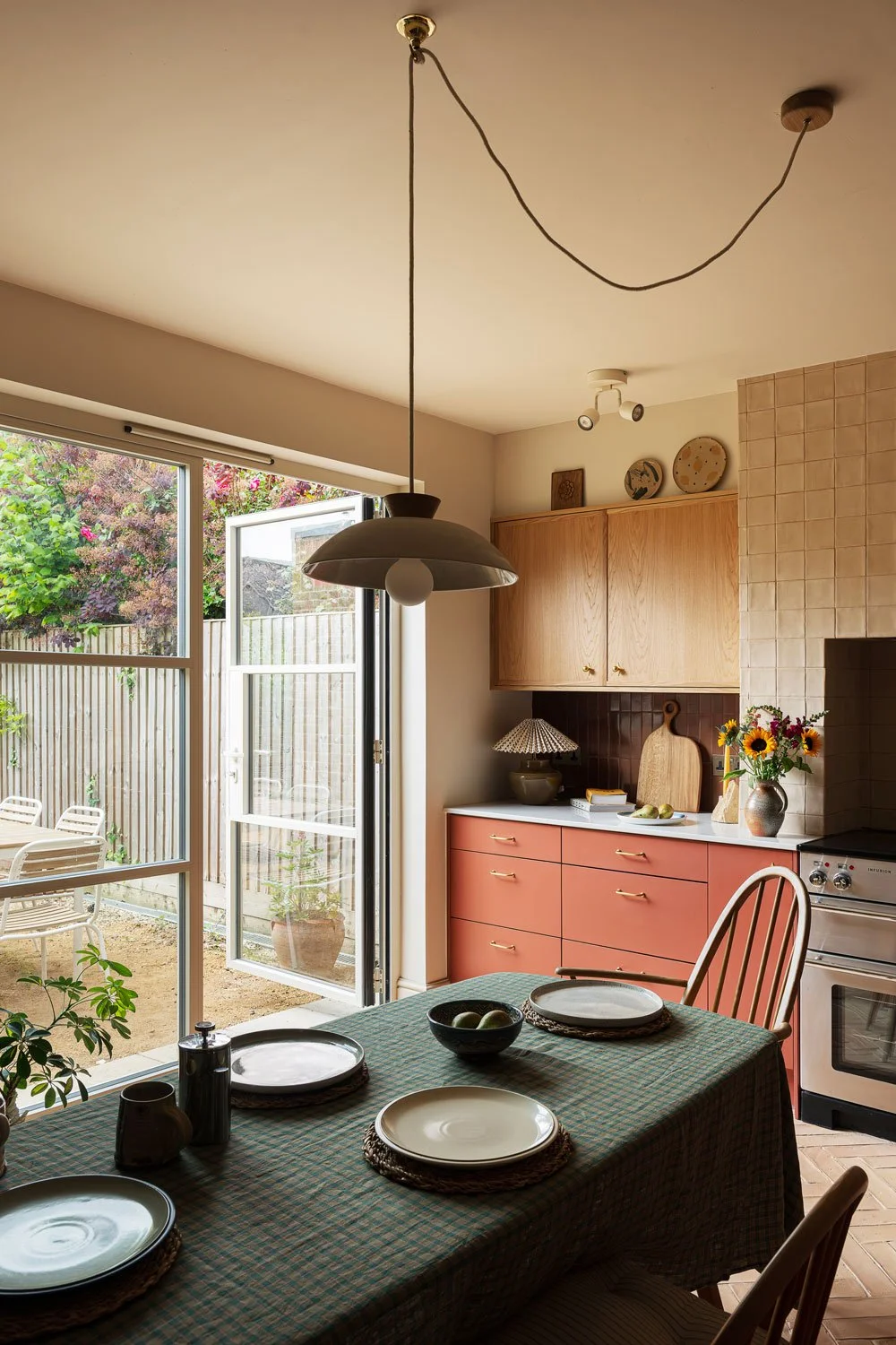 A contemporary kitchen design in Knowle, Bristol. Warm oak and bold red cabinetry combines with handmade zellige tiles to create a characterful space with views through the cream crittal doors out the garden