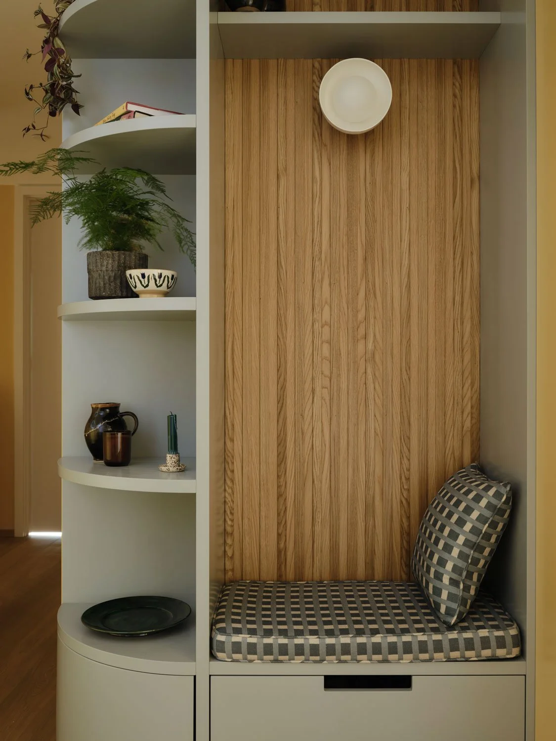 An entrance bench with oak slatted back and curved shelves create a welcoming entrance to this apartment. The open shelves provide a place to display treasured items