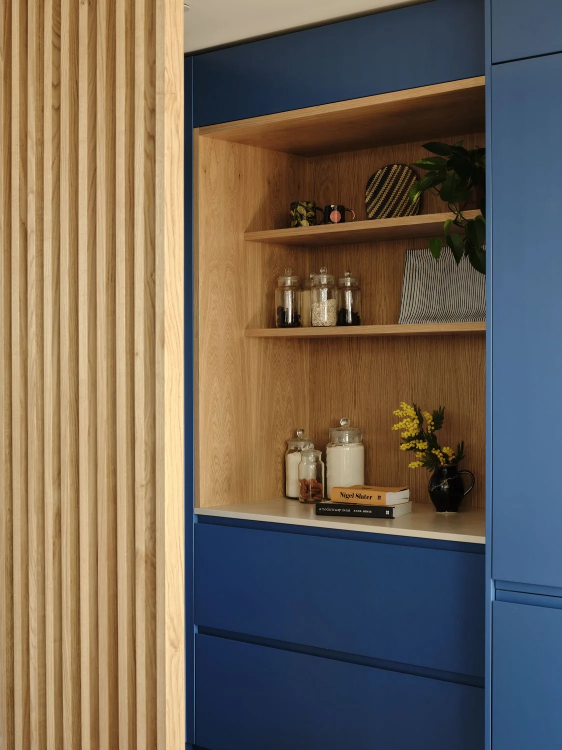 A detail image of a bold blue kitchen with oak pantry unit and elegant oak slatted screen
