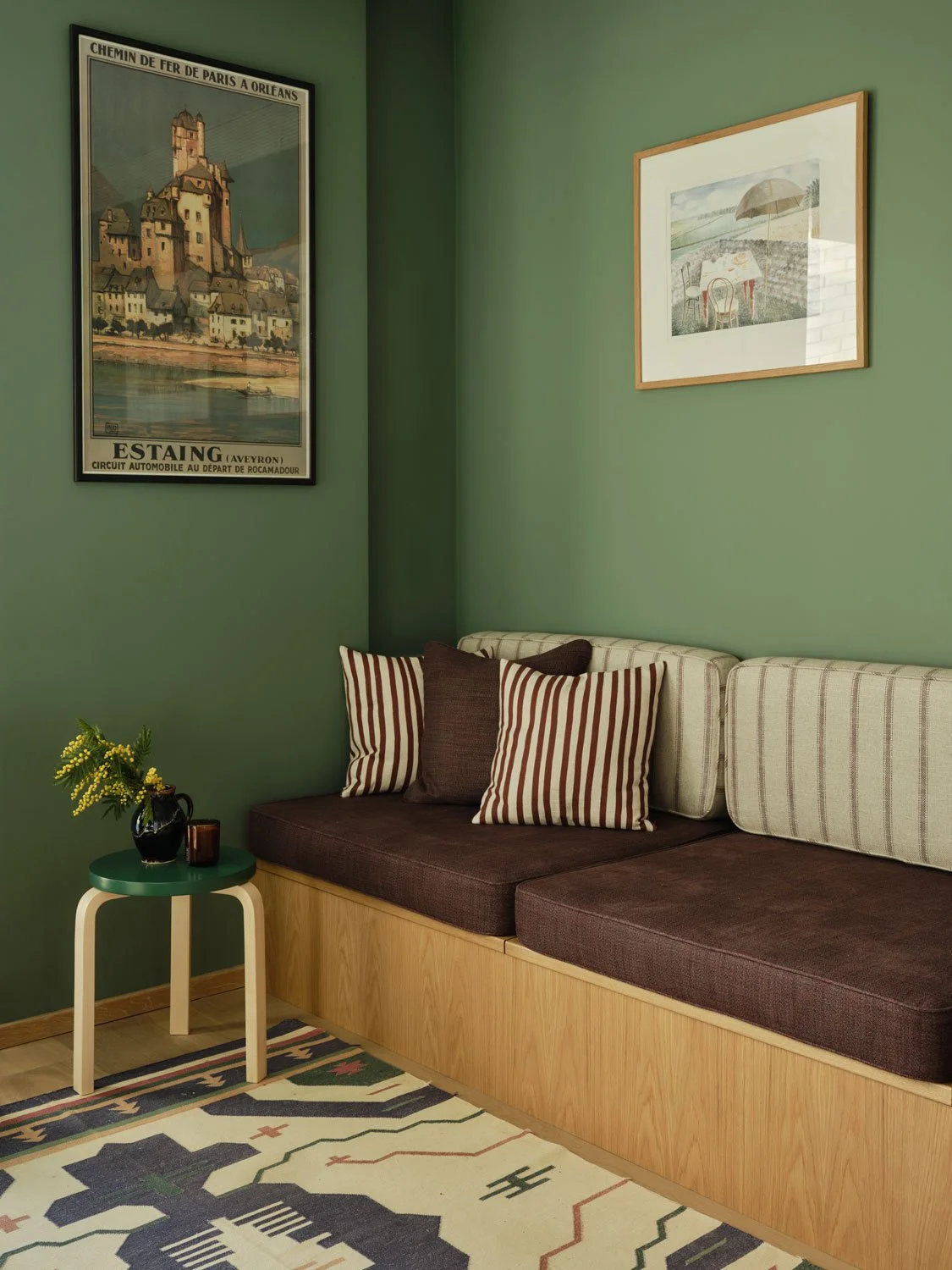 A bold green living room with bespoke built in oak day bed provides storage and a place for guests to stay. Rich maroon fabrics create a bold contrast to the green walls