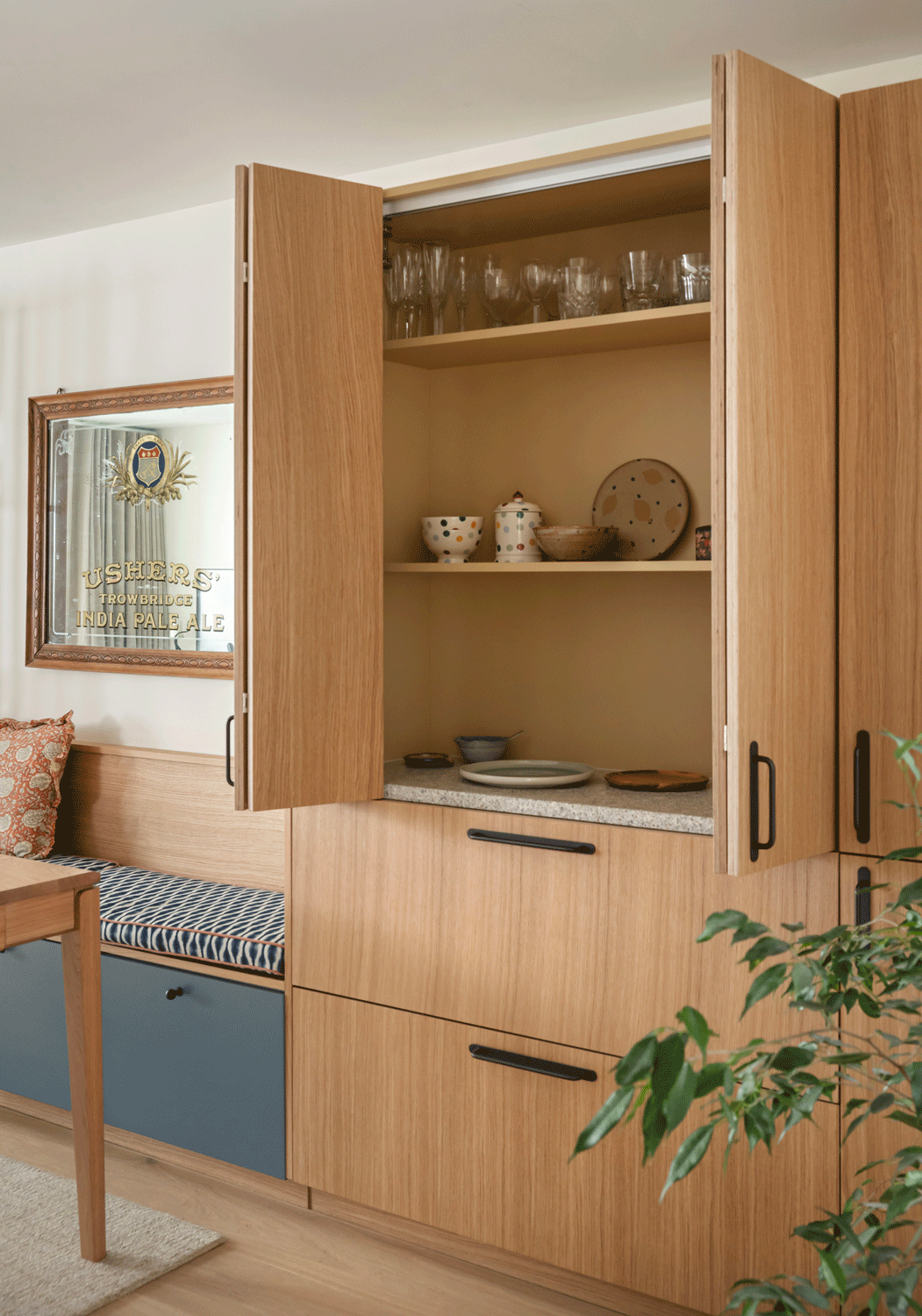 An oak kitchen pantry unit sits alongside a built in blue dining bench with bold patterned fabric cushion