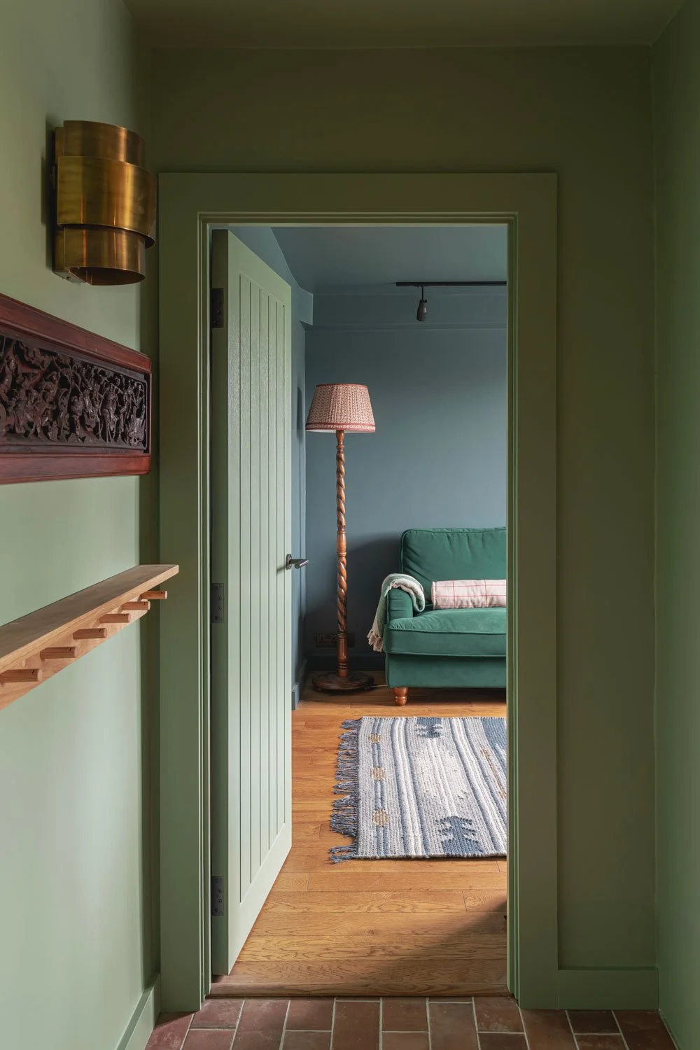 A grren hallway with terracotta tiles leads in to a cosy blue snug with a green velvet sofa