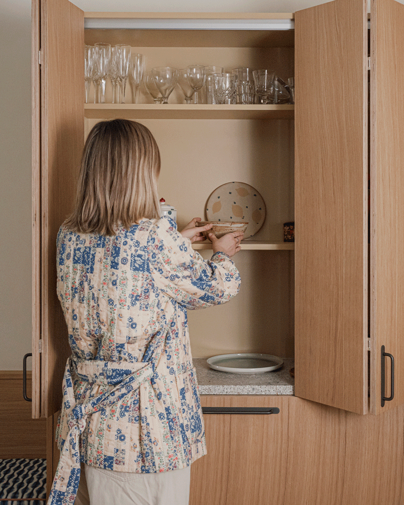 A designer styling an oak pantry unit with warm yellow interior