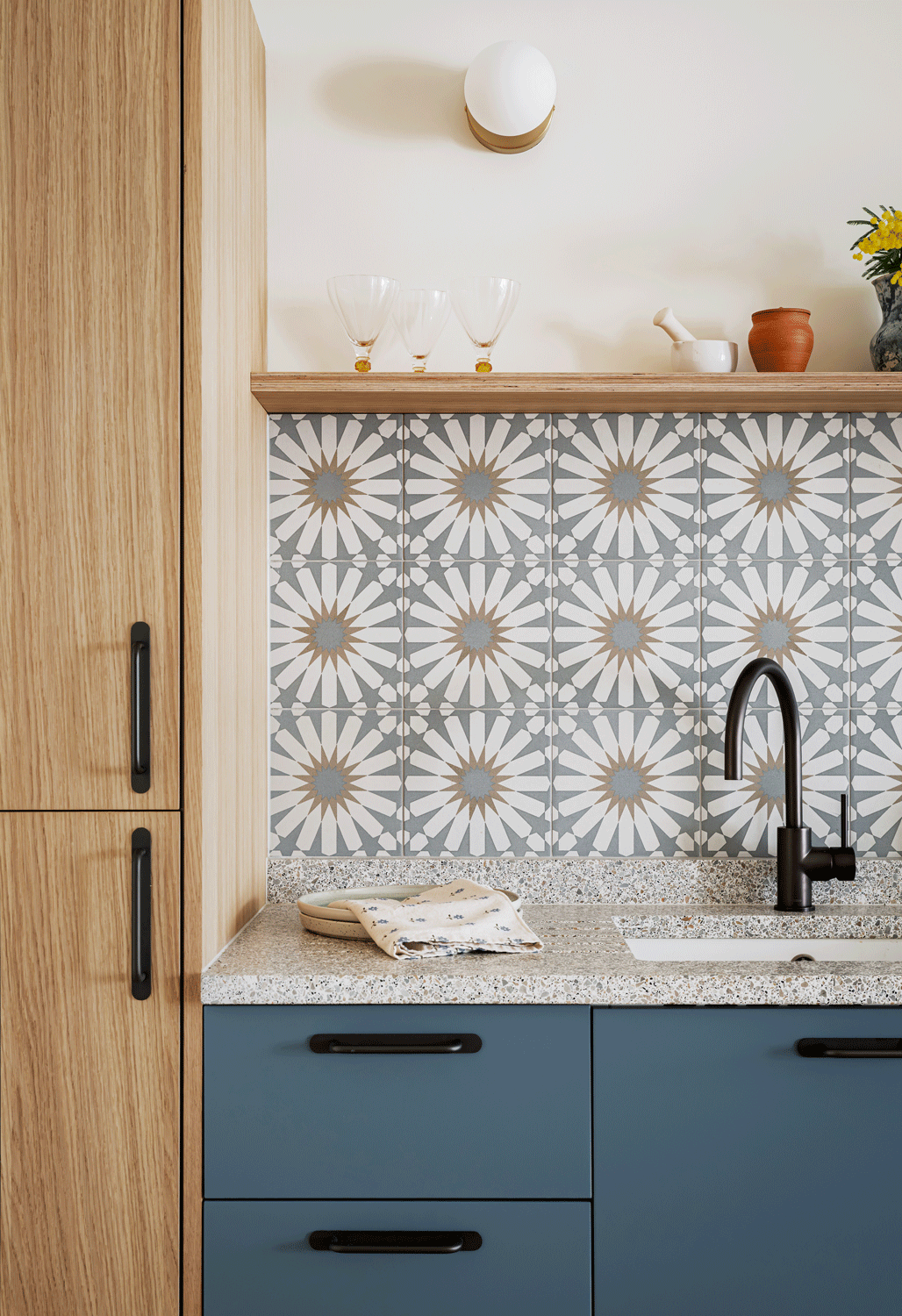 Oak and bright blue cabinets are combined with a pretty speckled terrazzo worktop and bold patterned backsplash tiles