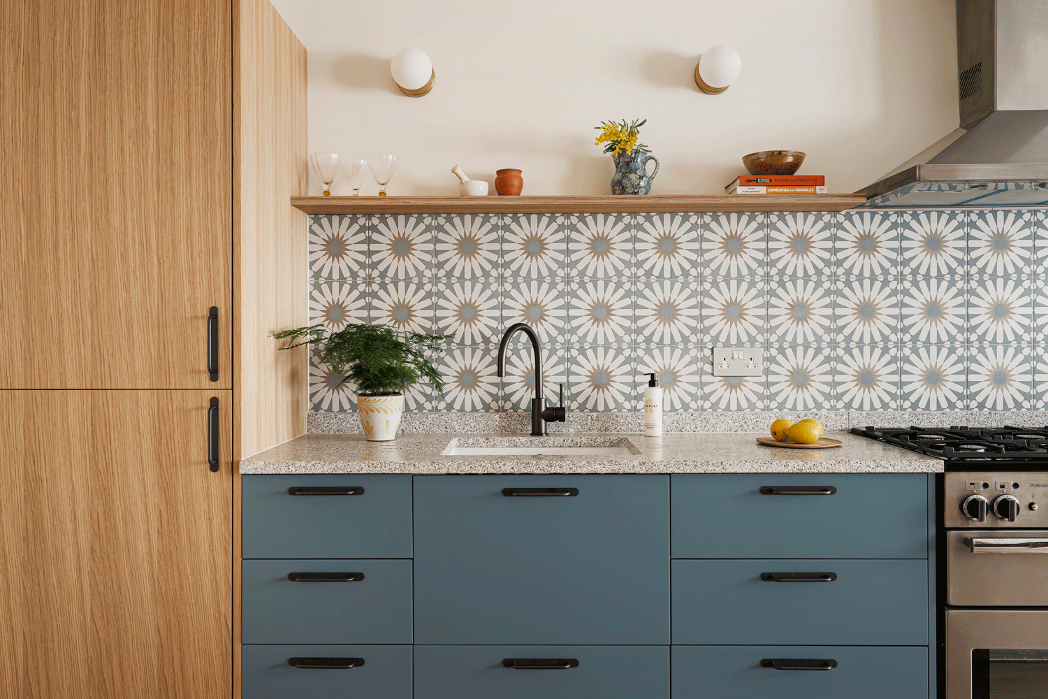 A warm oak and bold blue kitchen with a speckled terrazzo worktop and bold patterned backsplash tiling. A deep bronze tap is complimented by the deep bronze handles