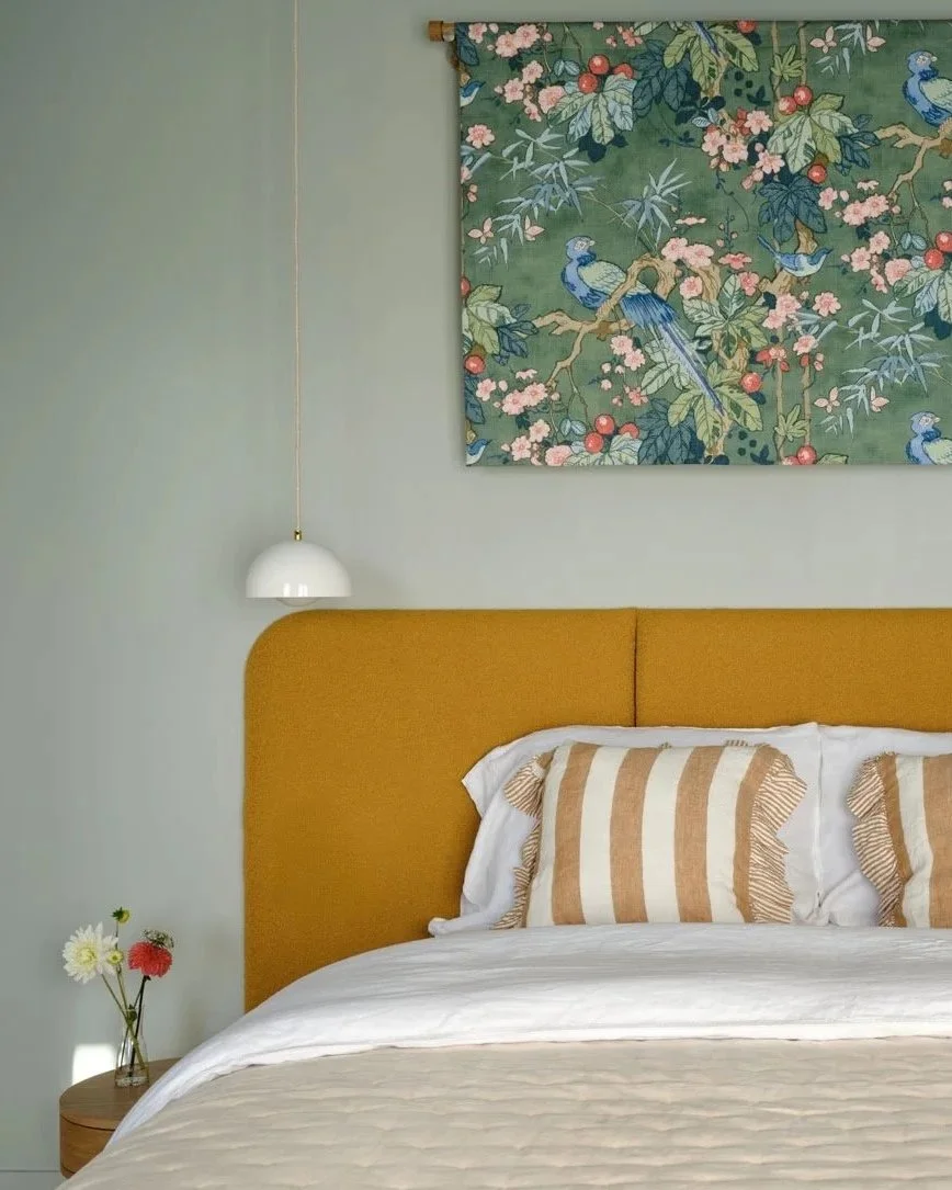 A bedroom with bespoke mustard headboard, striped yellow cushions and a bespoke floral fabric wall hanging