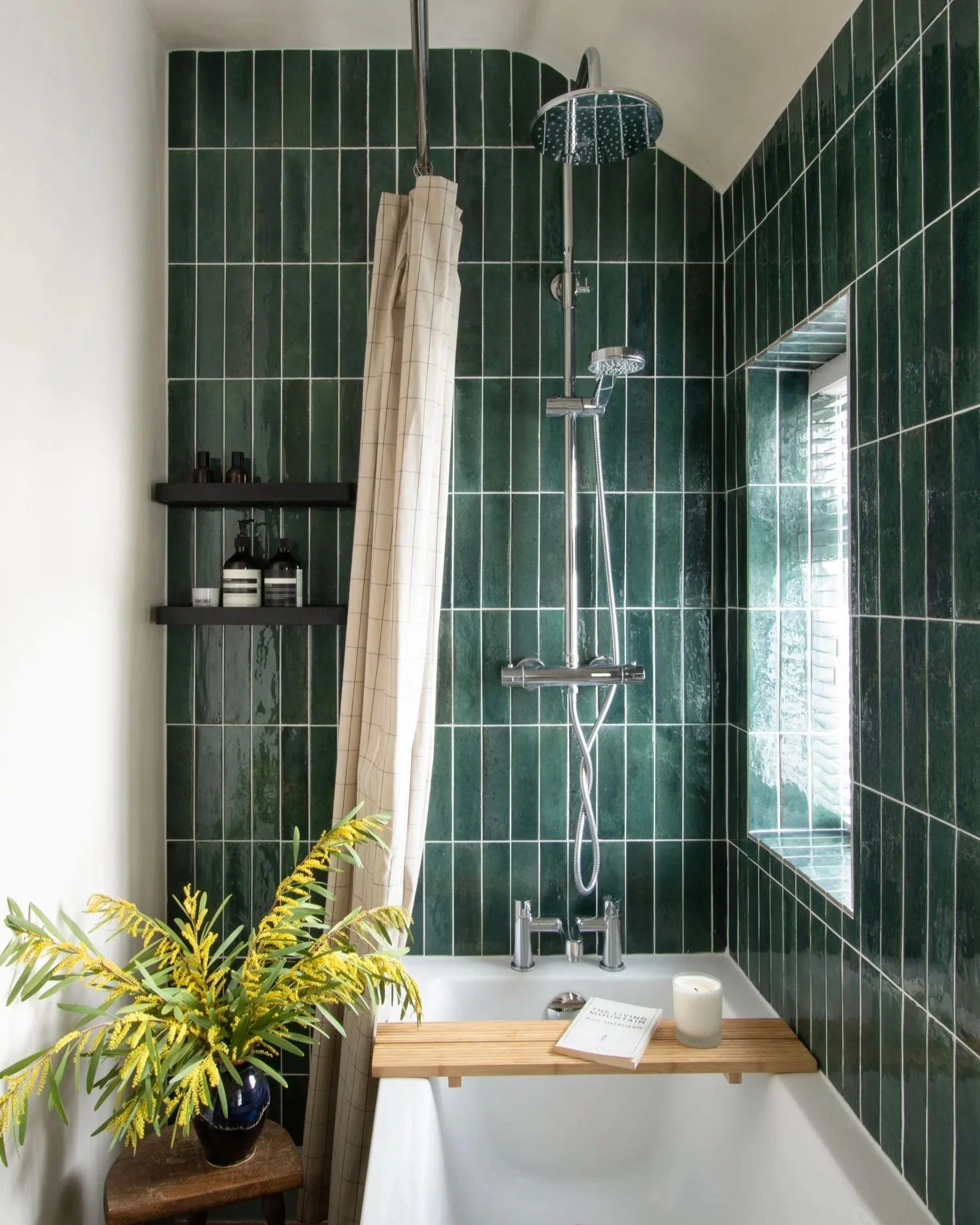 A green tiled bathroom with textural fabric shower curtain styled with yellow flowers. A tranquil bathroom space