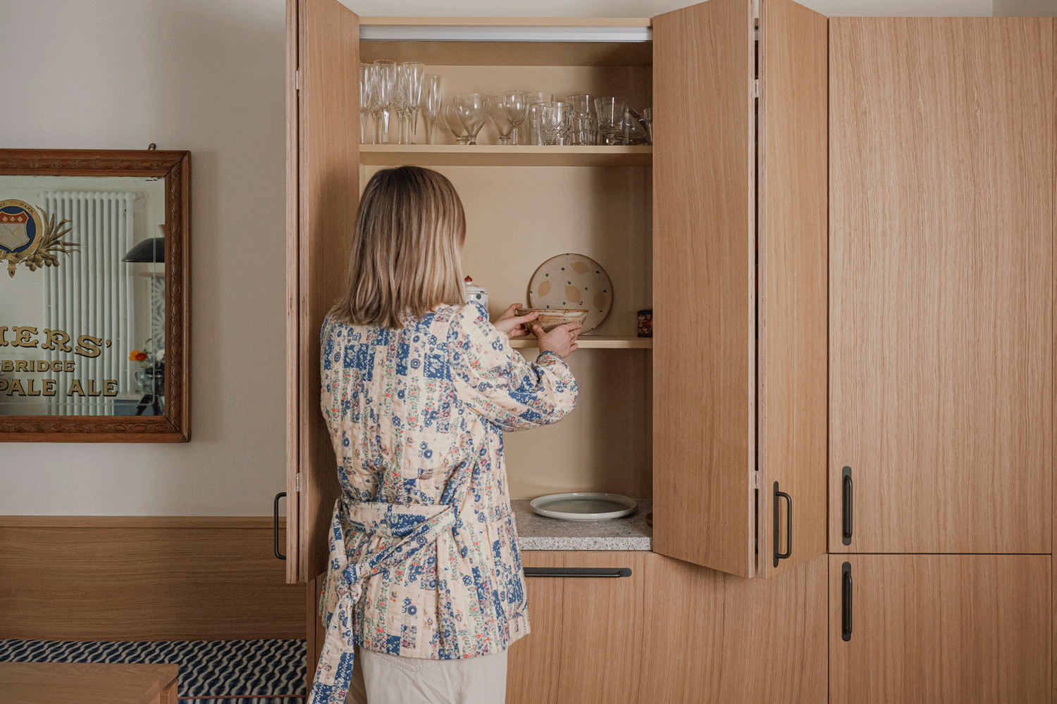 A designer is styling an oak pantry unit in a small kitchen