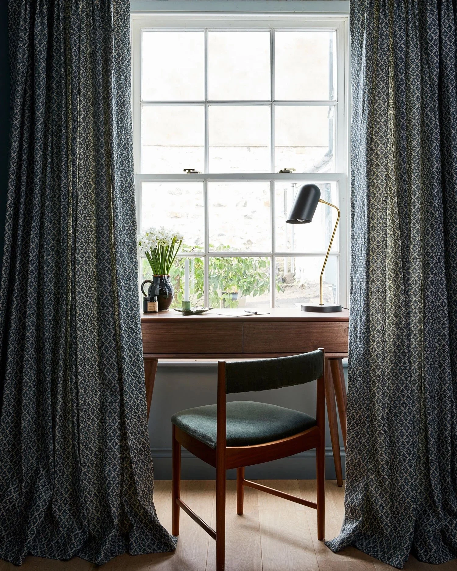 Desk nook in window with patterned blue curtains and a mid century desk and velvet side chair