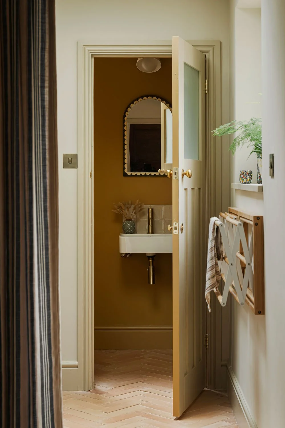 A contemporary kitchen in Knowle, Bristol with a view through to a mustard yellow cloakroom with brass tap ware and a curved scalloped mirror