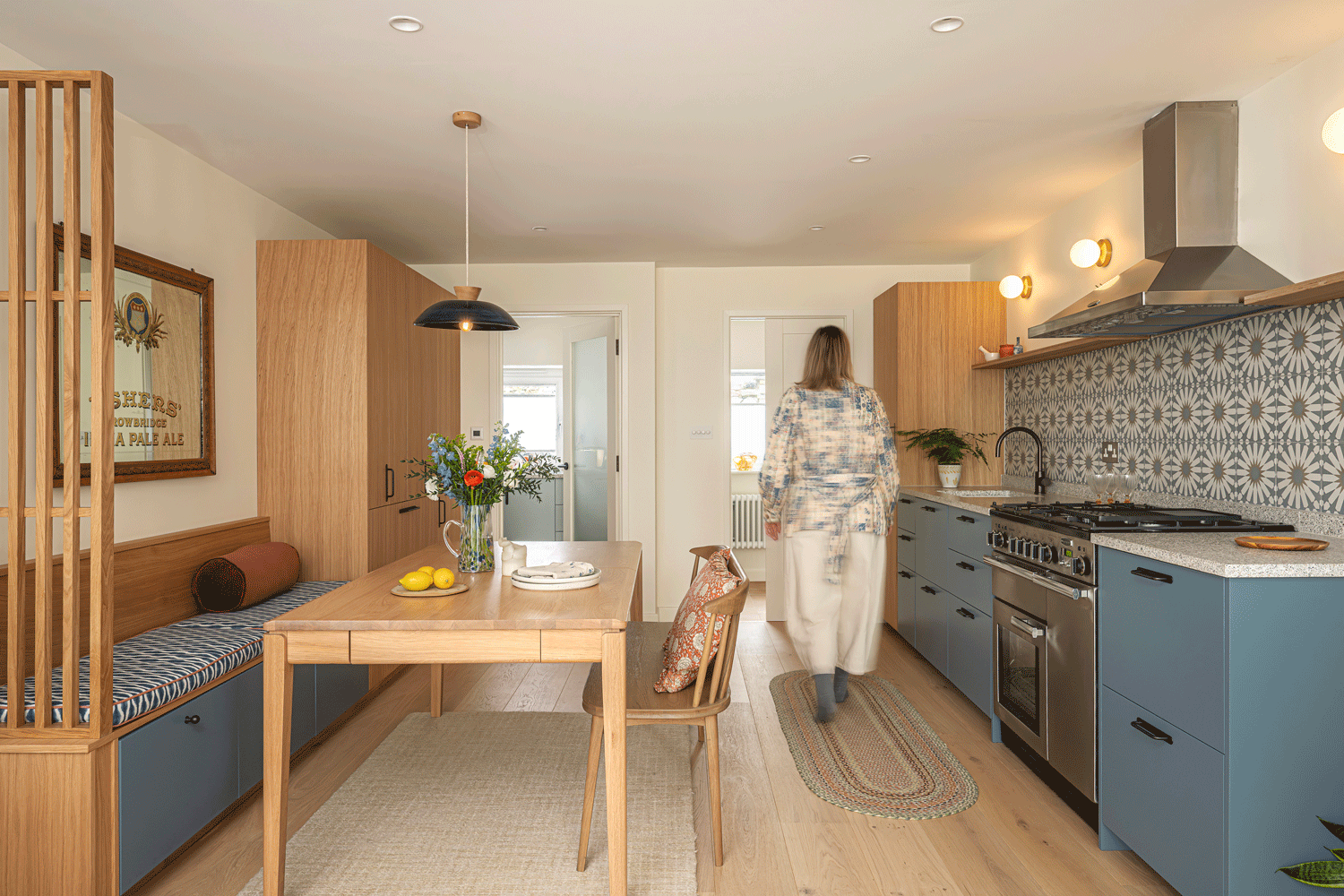 A spacious compactful kitchen dining space combining warm oak and bold blue cabinetry with a bold patterned backsplash tile