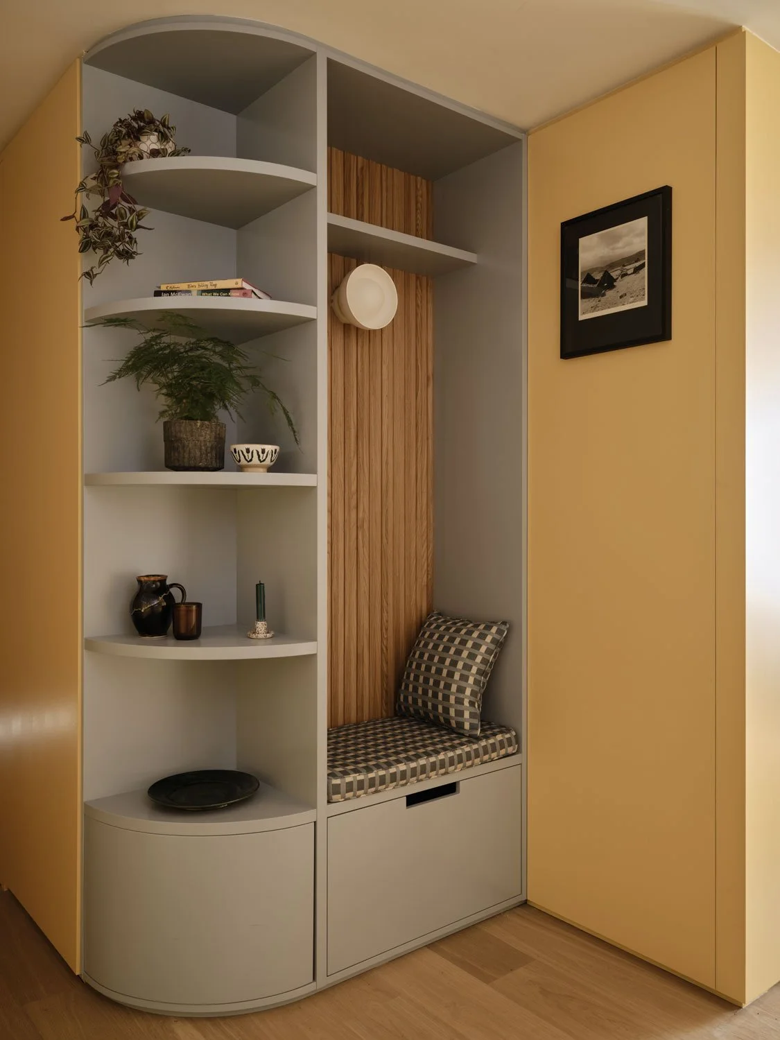 A light blue entrance bench with curved shelves create a welcoming entrance to this King's Cross apartment. Oak slats add texture and warmth. Imogen Heath patterned fabric cushions add a playful fee