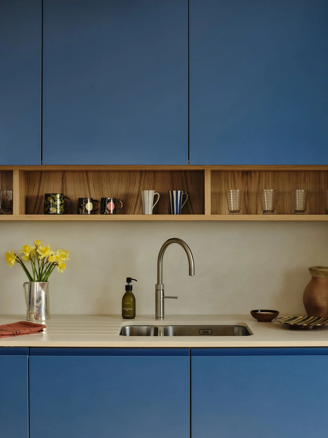 A detailed image of a kitchen worktop and bold blue cabinets with oak open shelving