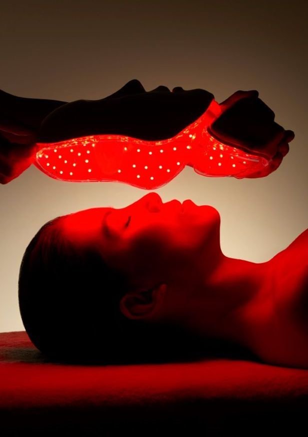 A person lying down with their head resting on a surface, holding a glowing red sneaker with small holes illuminated from within, appearing as if they are about to kiss or touch the shoe.