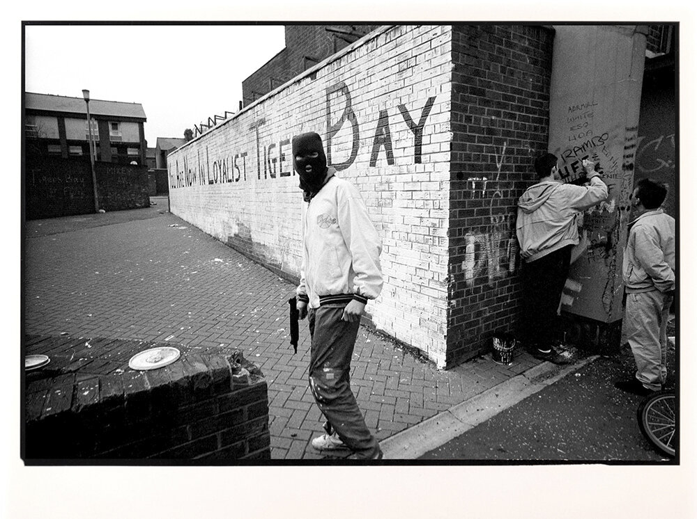  A hooded paramilitary gunman stands in front of a painted wall that reads, You Are Now In Loyalist Tiger Bay, in Belfast, Northern Ireland. 1990 