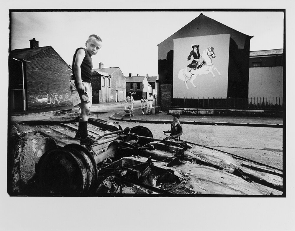  Children play in the burned-out remains of a car torched the night before in a riot between Catholics and Protestants in Tiger's Bay, Belfast, Northern Ireland. 1989  These images are excerpts from    No Surrender: The Protestants   , self-published