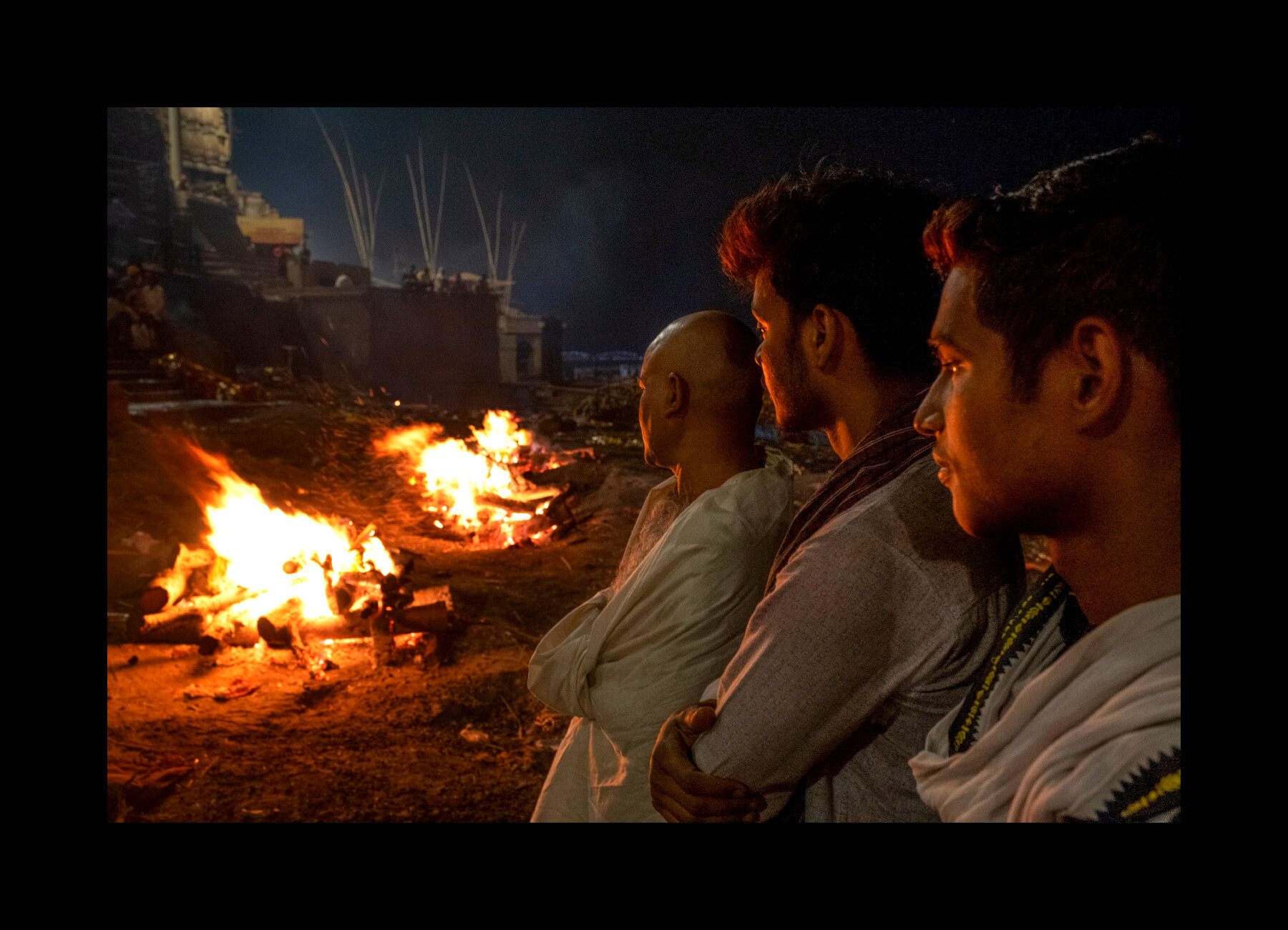  Men mourn the death of their 101-year-old father as the funeral pyre burns in the background at the Manikarnika Ghat in Varanasi, India. 2019 