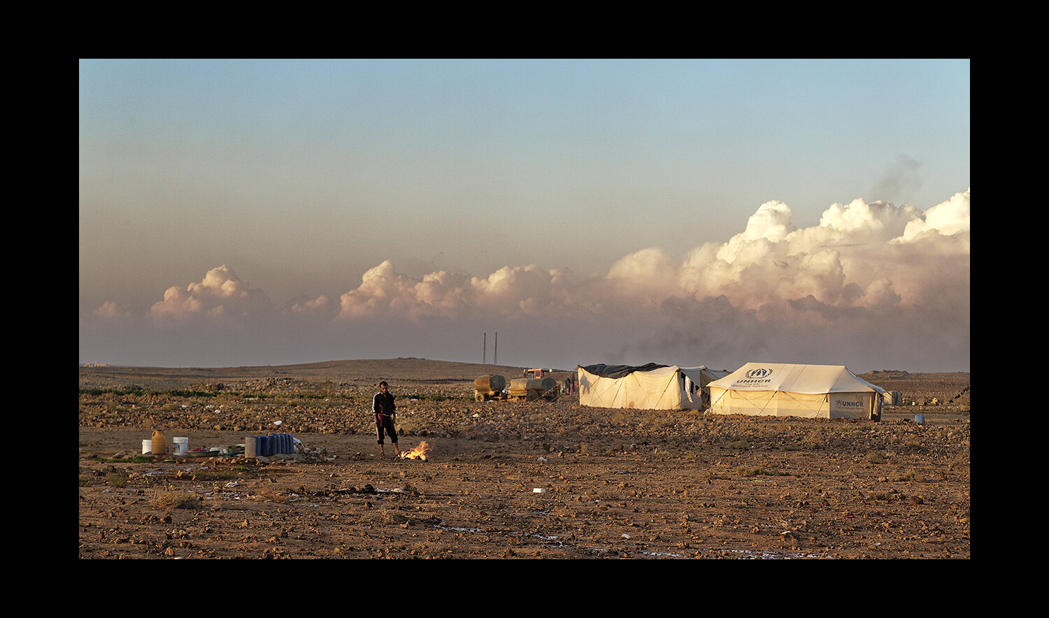  A refugee stands over a fire in an isolated enclave of tents in the desert of Ereinbeh, Jordan. 2013 