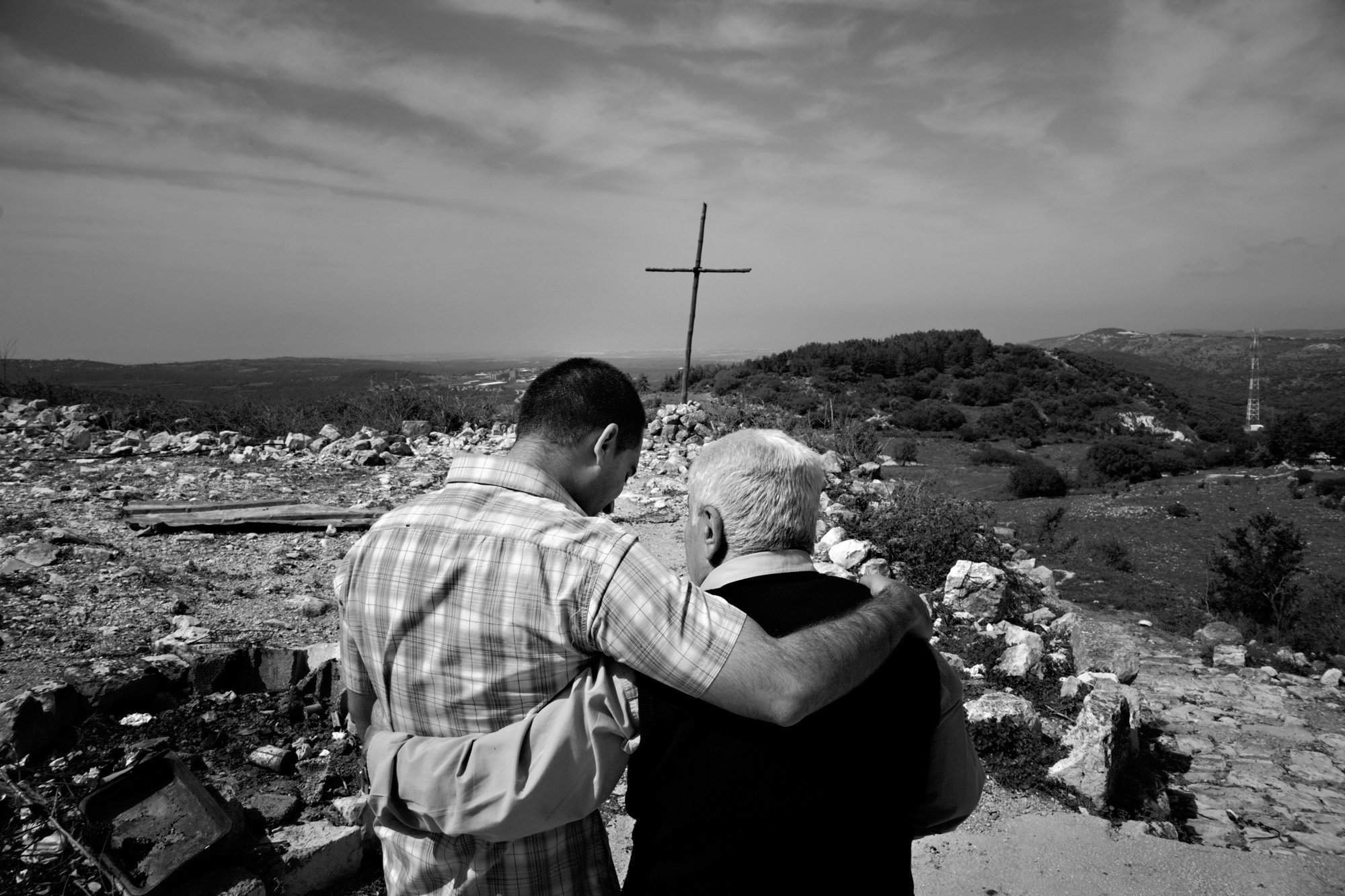  Two men console each other in front of a cross at their old church in Iqrit, in northern Galilee, Israel, on April 5, 2008. This Christian village was occupied by the Israeli military in 1948, and in 1951, they bombed it and destroyed all but this c