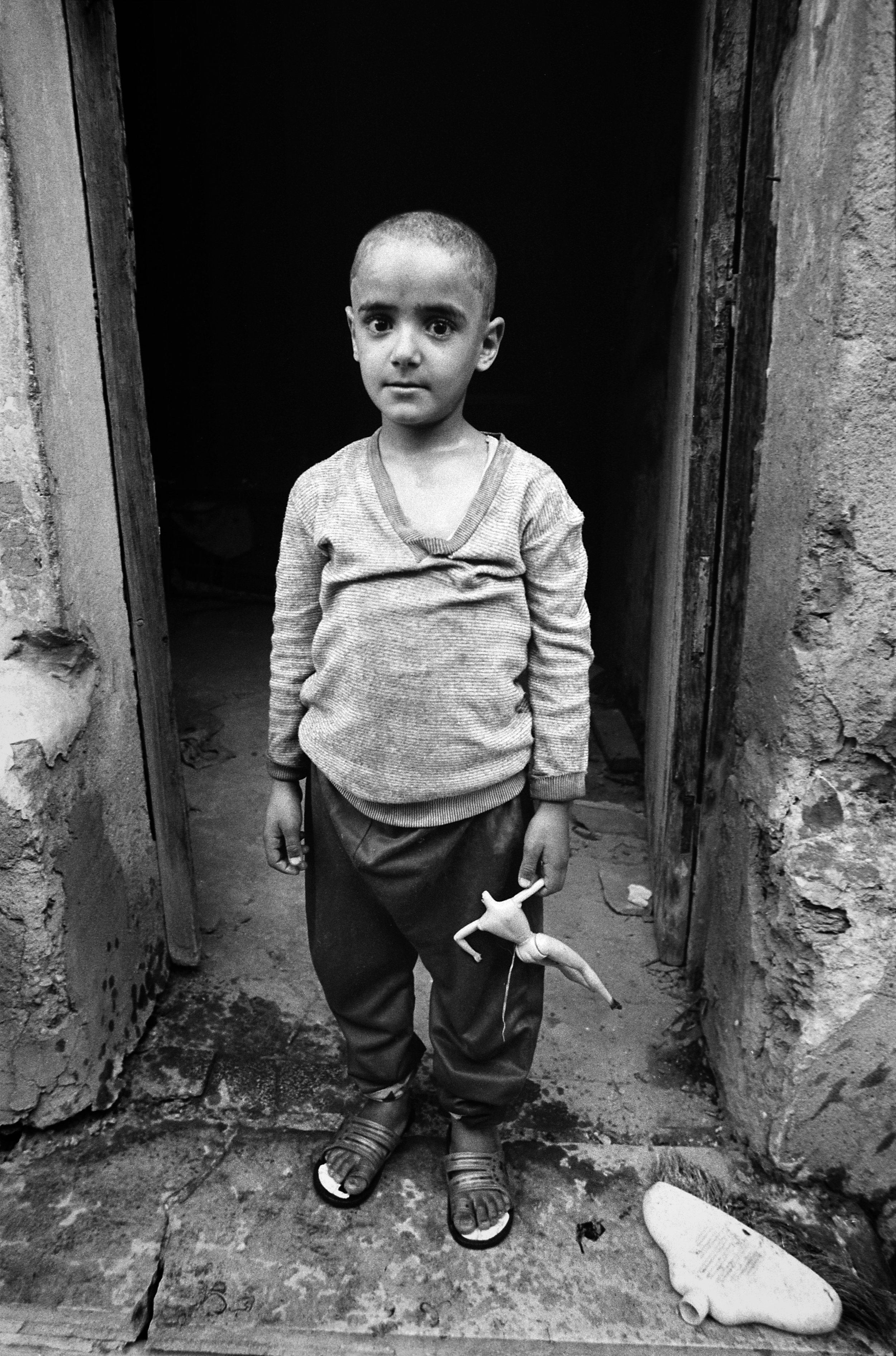  A young boy holds a broken doll in the doorway of the mausoleum where he and his family live. 