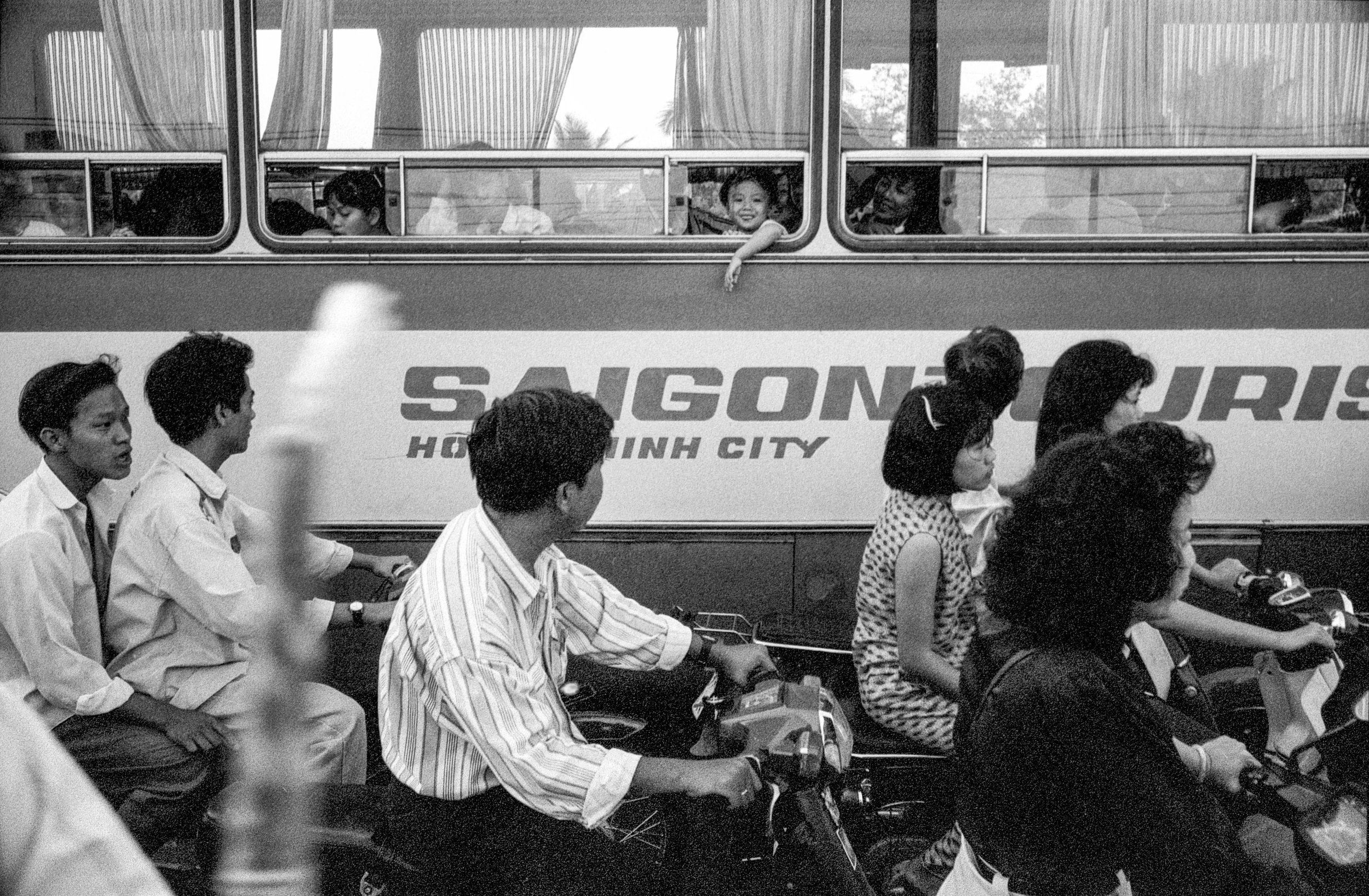  A young boy on a bus looks out the window and smiles, as traffic grinds to a halt in the streets of Saigon.  