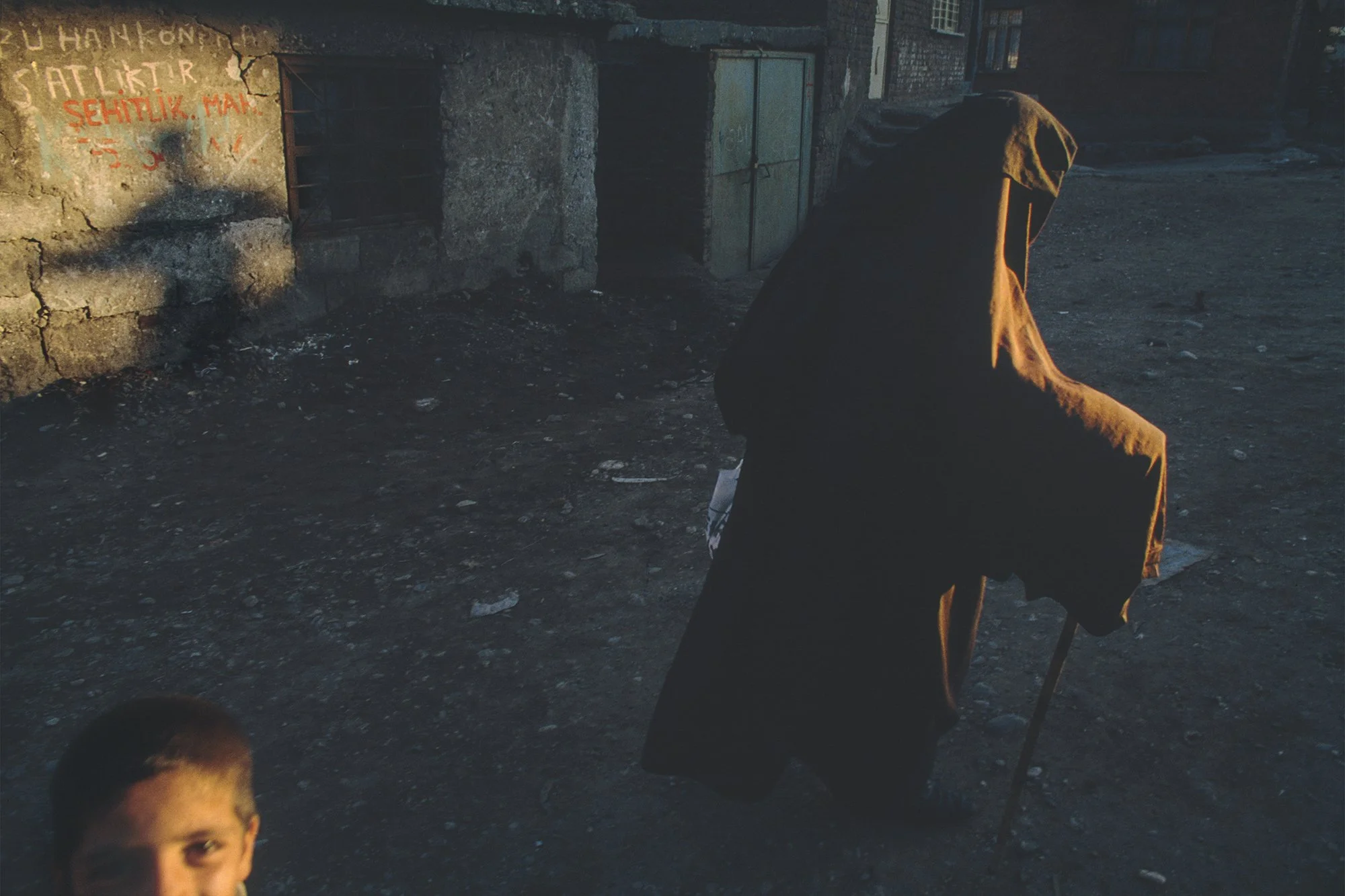 A young boy looks to the camera while a mysterious, robed figure walks by in the Ali Pashi district of Diyarbakir, Turkey on Nov. 11, 1991
