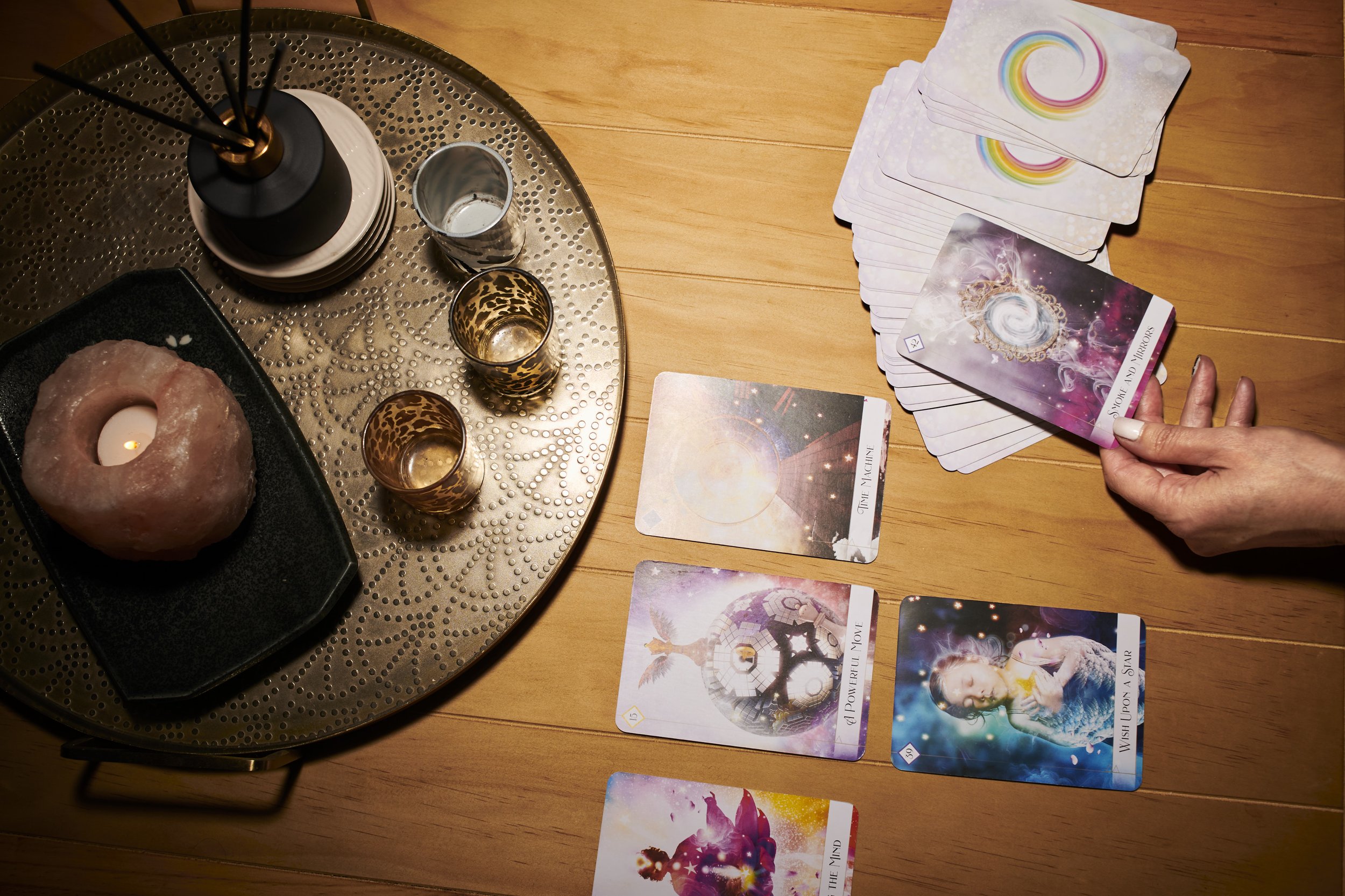 Hands laying out illustrated cards on a wooden table beside candles