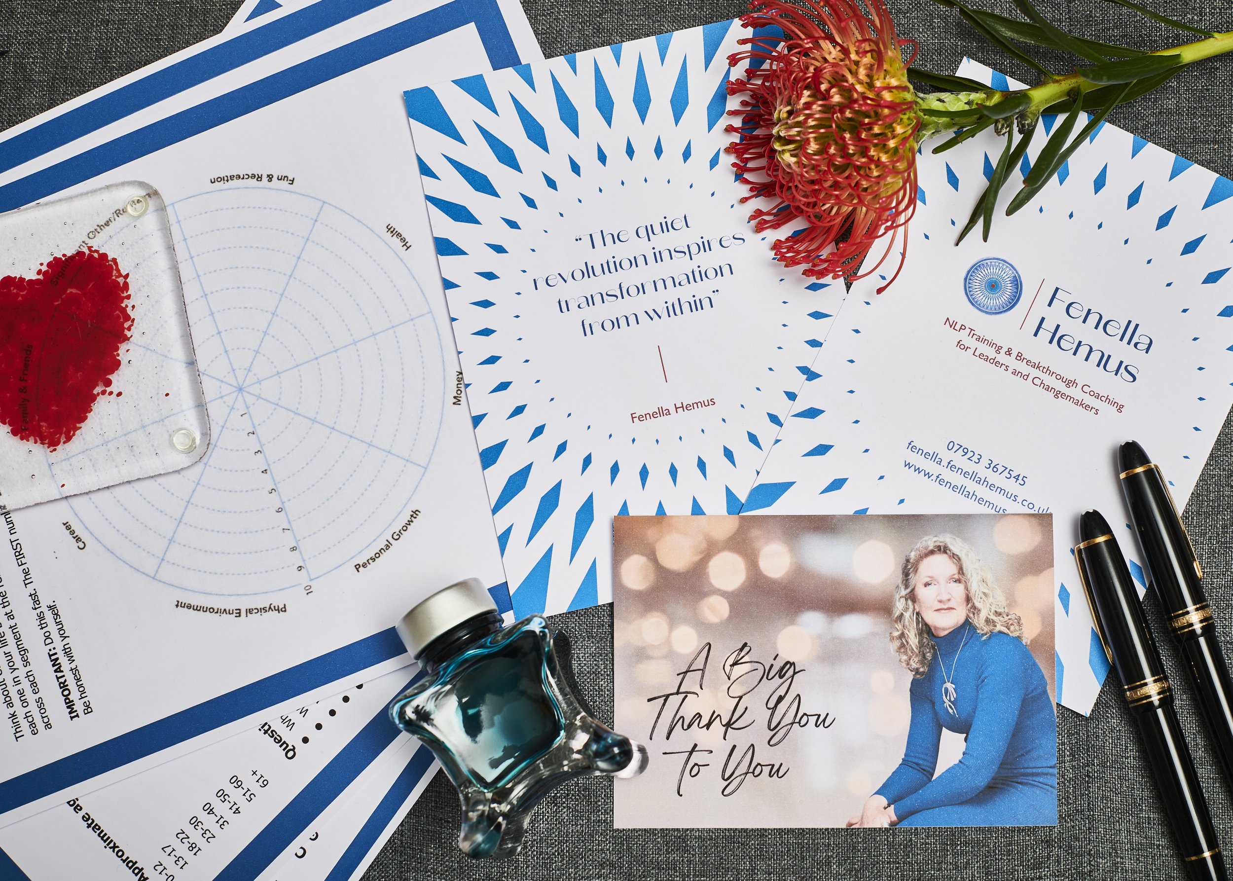 Flat lay of printed coaching cards, a thank-you postcard, fountain pens, an ink bottle and a red protea flower