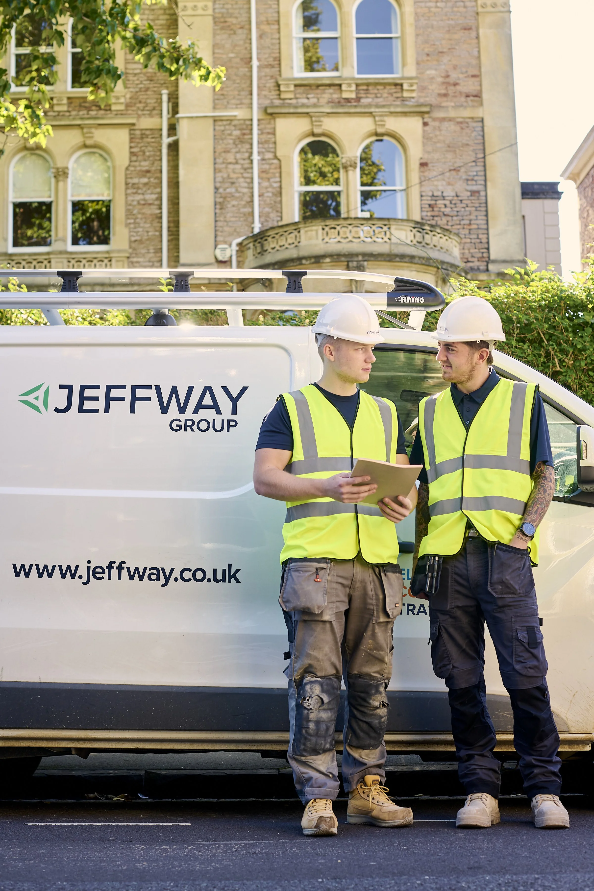 Two Jeff Way Group engineers in hi-vis checking notes beside a branded company van