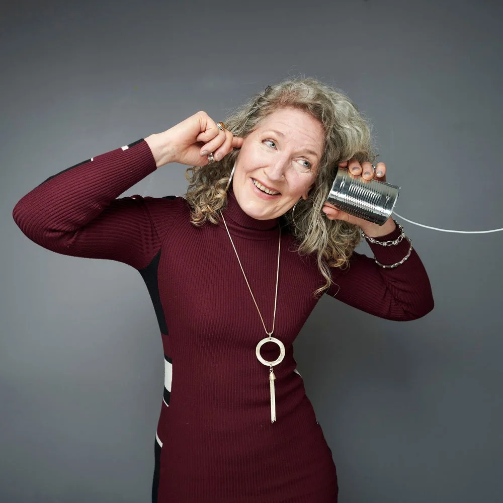 Woman in a burgundy dress smiling as she holds a tin-can telephone to her ear