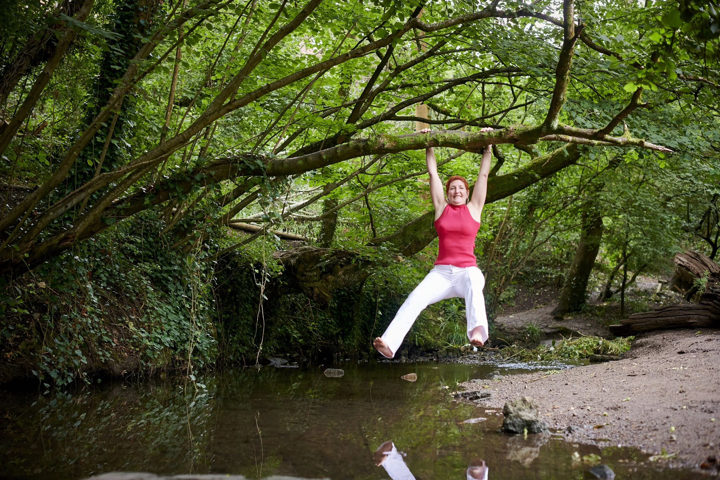 Woman hanging from a tree branch above a woodland stream