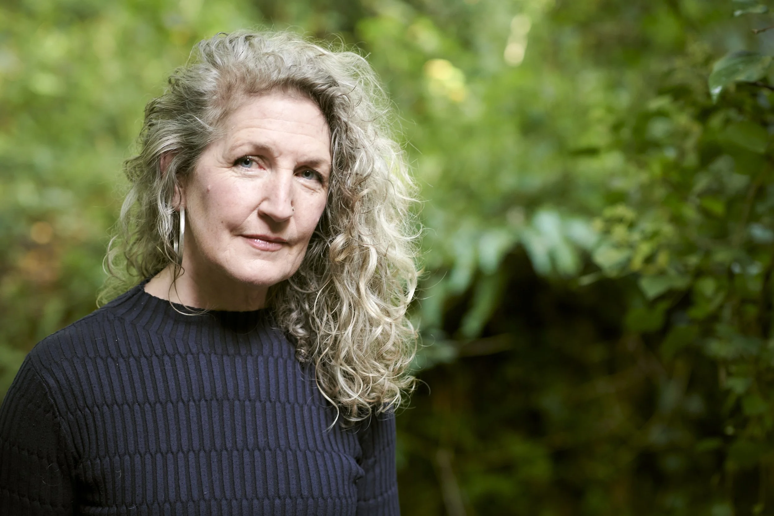 Outdoor portrait of a woman in a navy jumper against green foliage