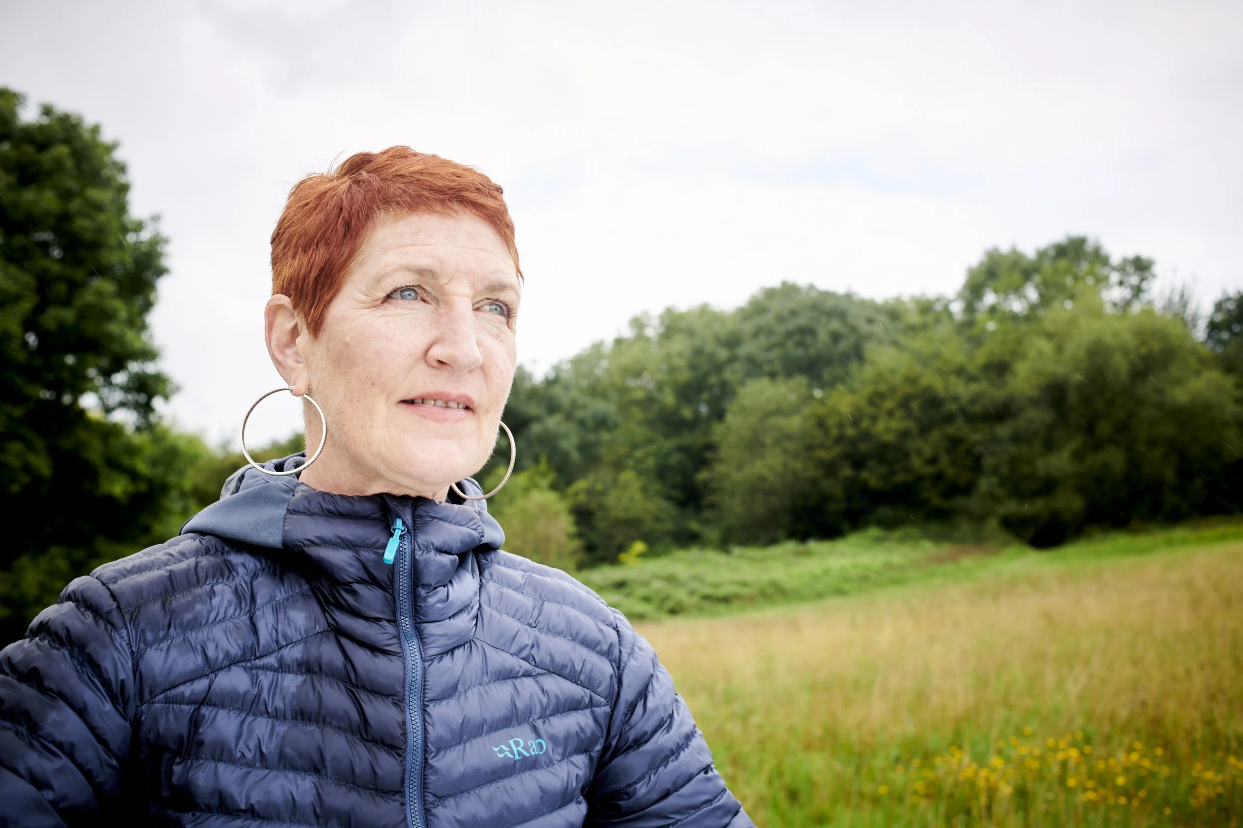 Woman in a navy puffer jacket standing in a field, looking off to one side