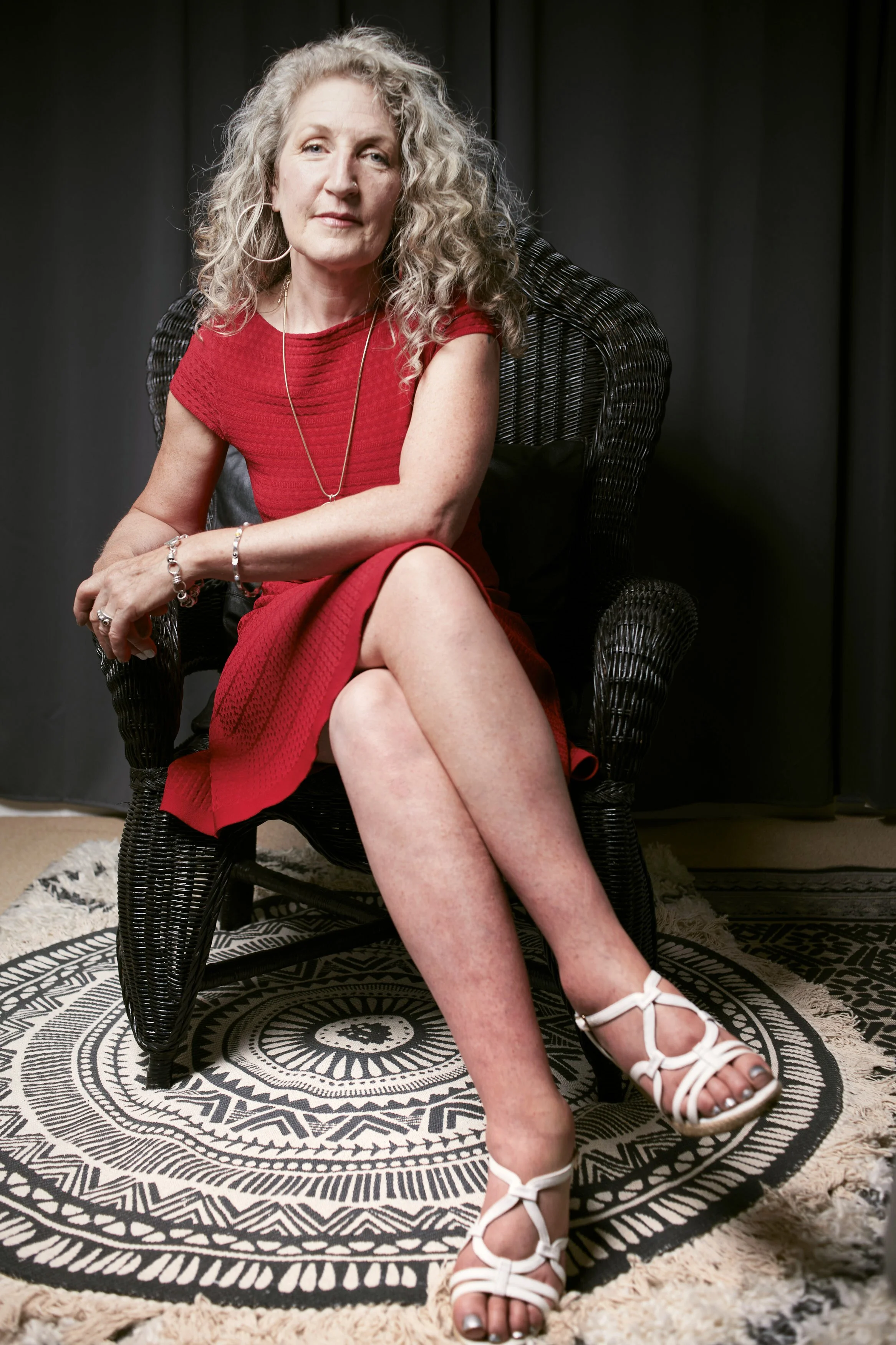 Woman in a red dress sitting in a wicker chair on a black and white patterned rug