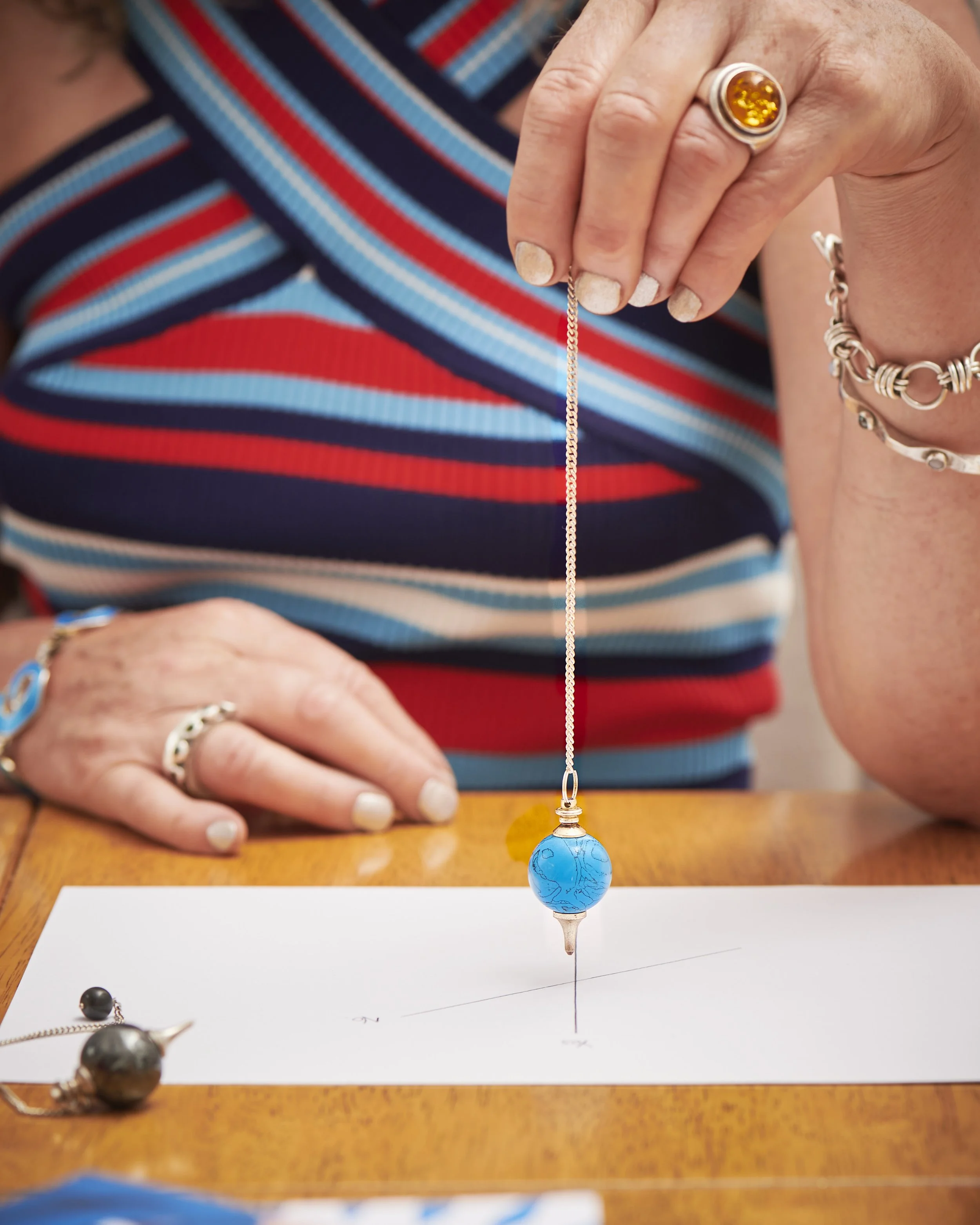 Close-up of a hand holding a blue crystal pendulum over a sheet of paper