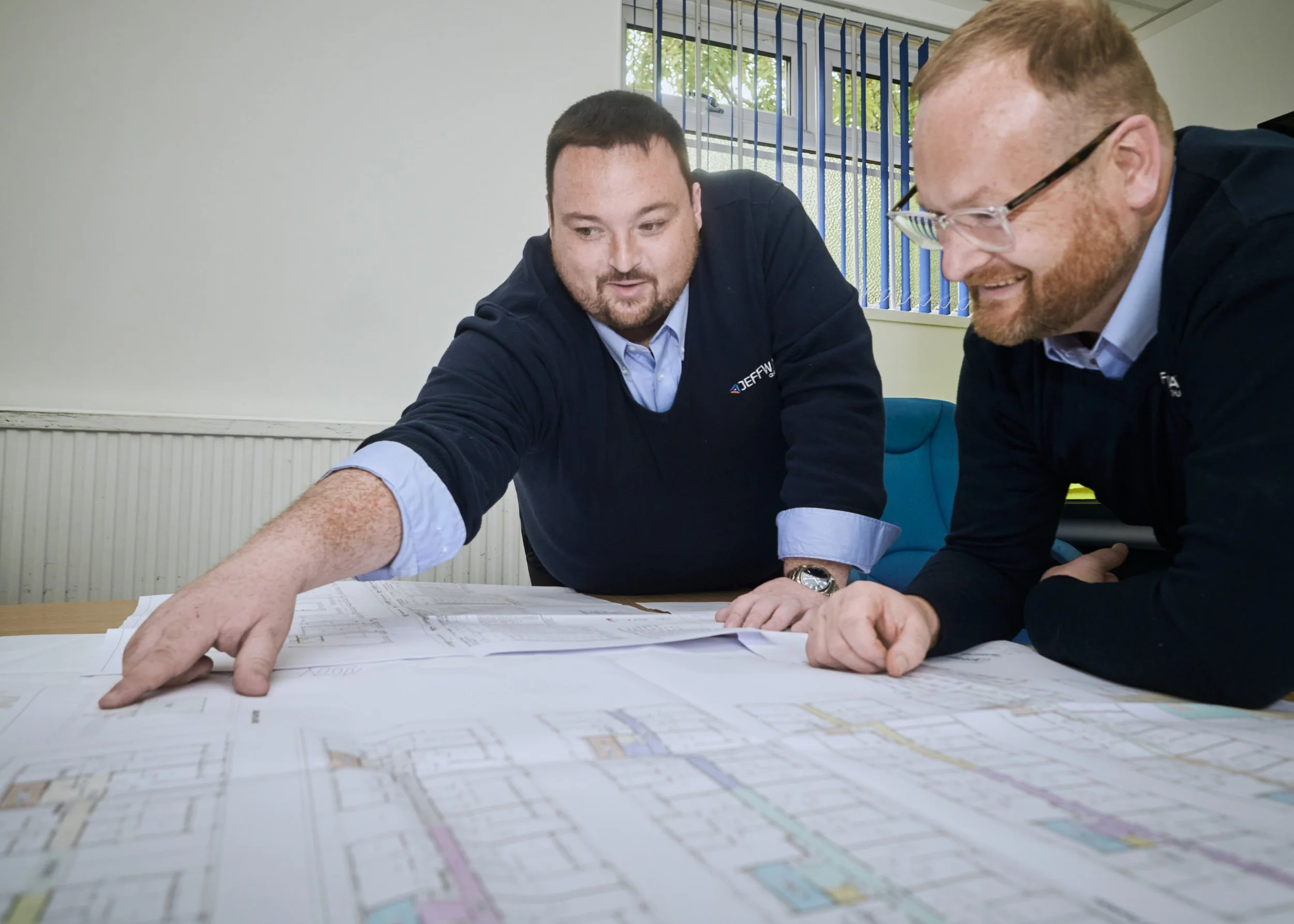 Two Jeff Way Group managers reviewing building plans on a table
