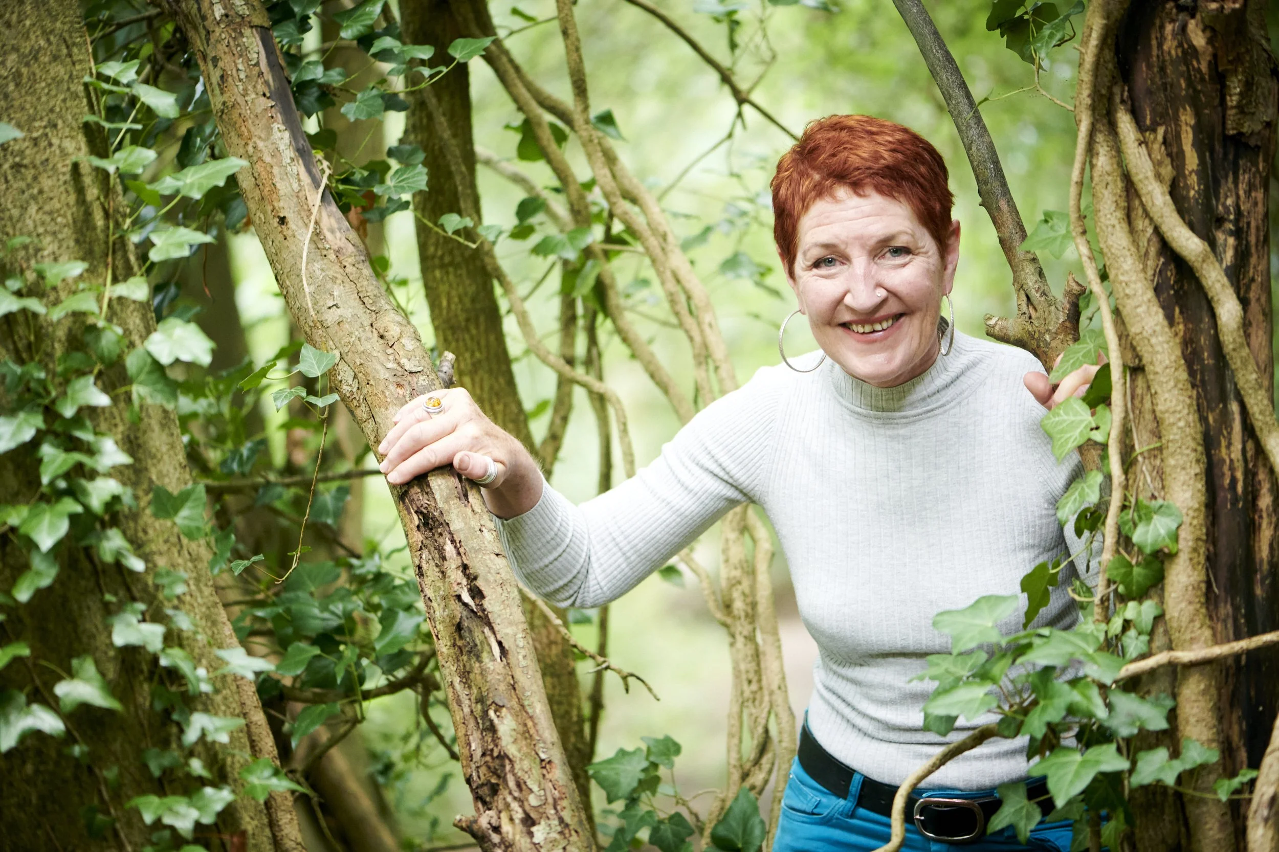 Woman with short red hair smiling among ivy-covered trees